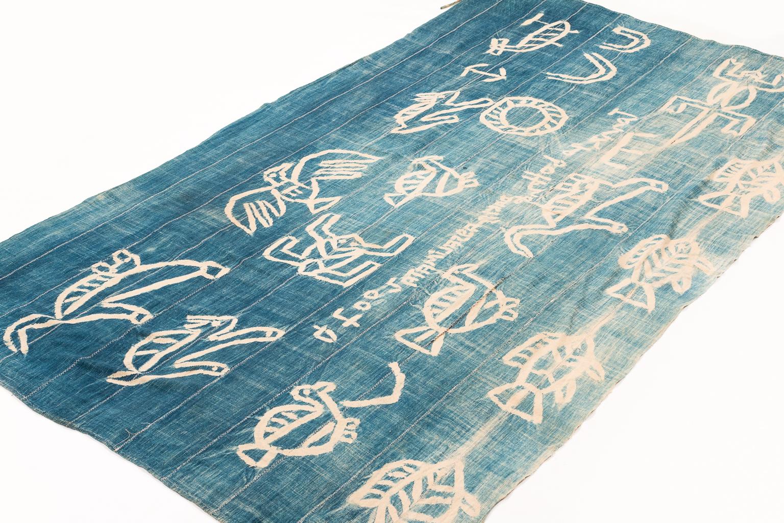 A resistance dye technique, similar to a hollandaise wax process, was used to create the animal motifs on this vintage tribal art blue and white ceremonial textile wrap. The gradient on the indigo shows beautiful variation. The cotton is very high