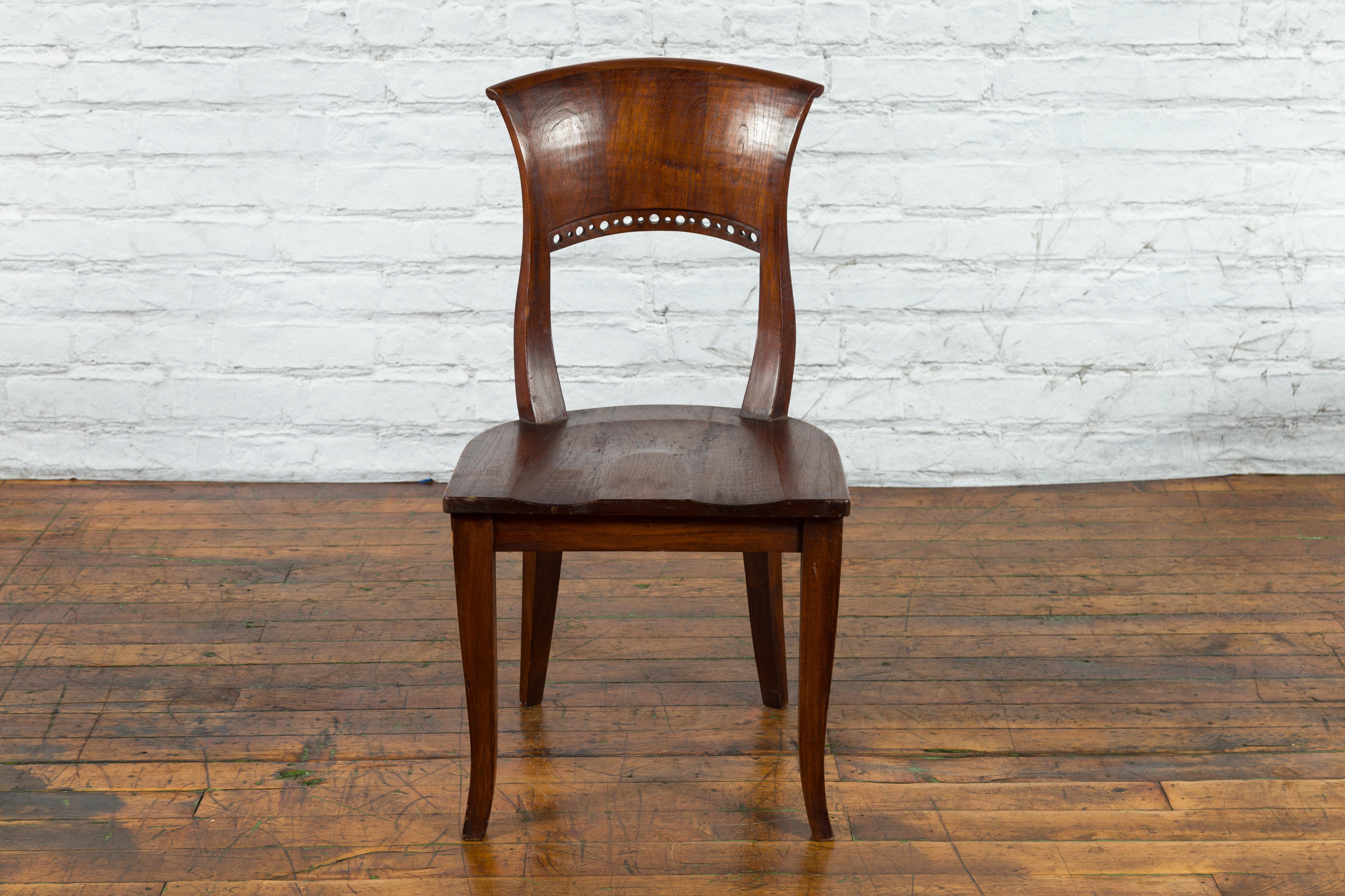 A vintage Indonesian wooden chair from the mid 20th century with pierced circular motifs. Created in Indonesia during the Midcentury period, this wooden chair features a curving back with out-scrolling upper rail and pierced circular motifs,