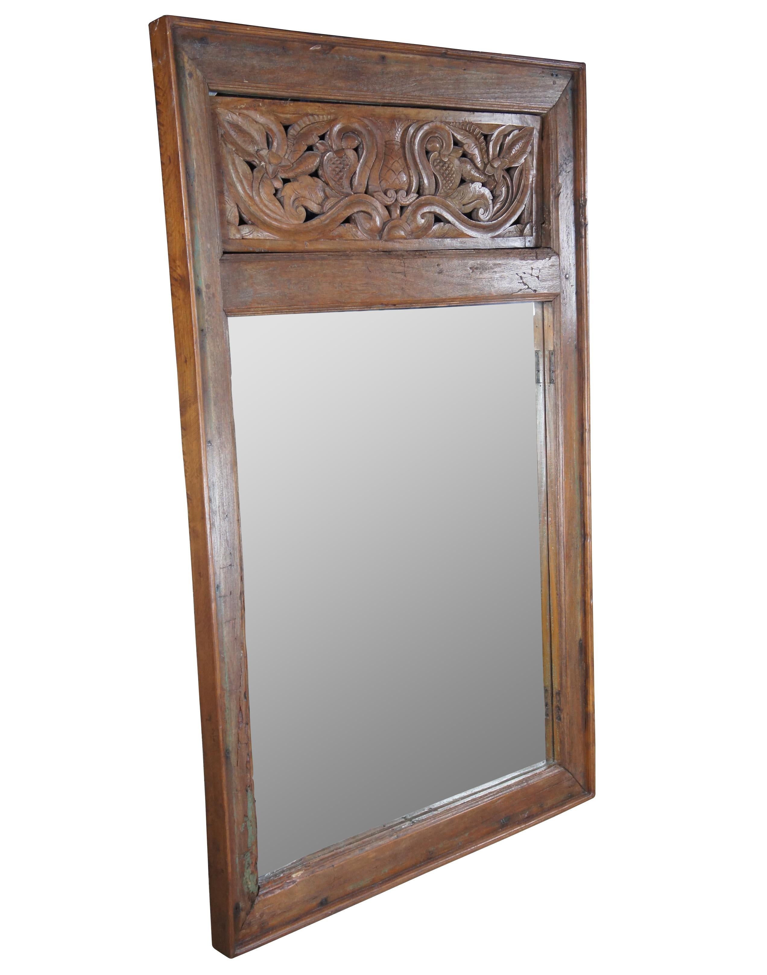 Impressive Indonesian carved mahogany over mantel or wall hanging mirror. Re-claimed or salvaged from a doorway or shutter. Original hinge marks can be seen along the inside of the trim. Features a rectangular frame with pierced foliate crown and