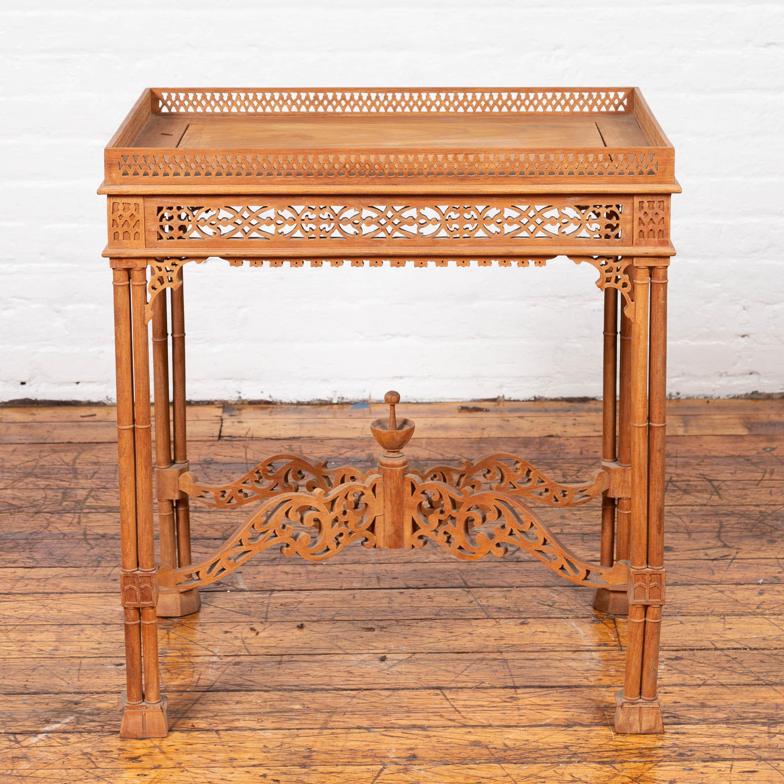A vintage Indonesian carved side table from the mid-20th century, with open fretwork design and cross stretcher. Our attention is immediately drawn to this side table's intricate carving. Featuring a rectangular tray top surrounded by a pierced