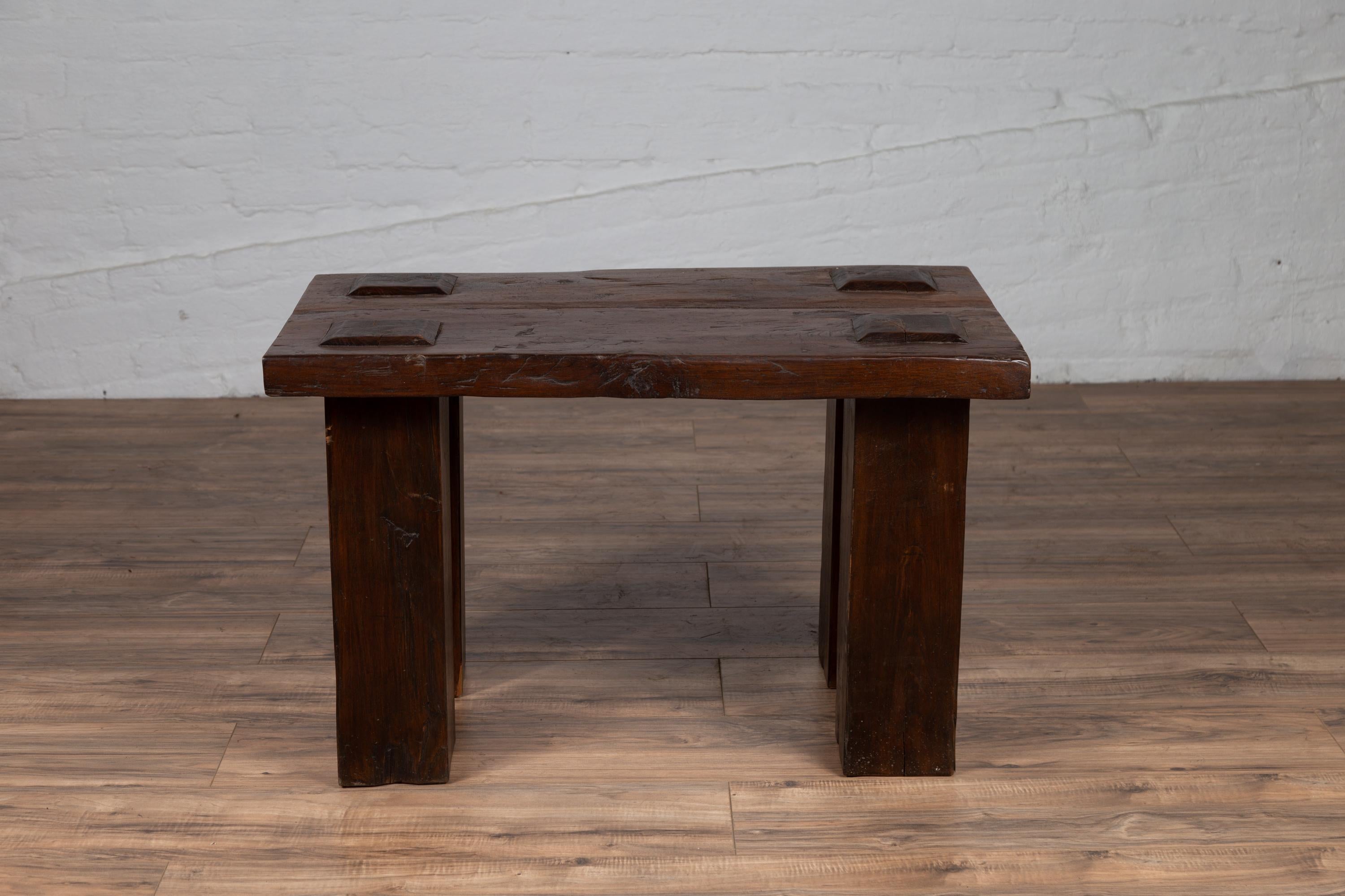 A vintage Indonesian wooden bench from the mid-20th century, with raised motifs and straight legs. Born in Indonesia during the midcentury period, this wooden bench charms us with its rustic presence and simple lines. Featuring a rectangular planked