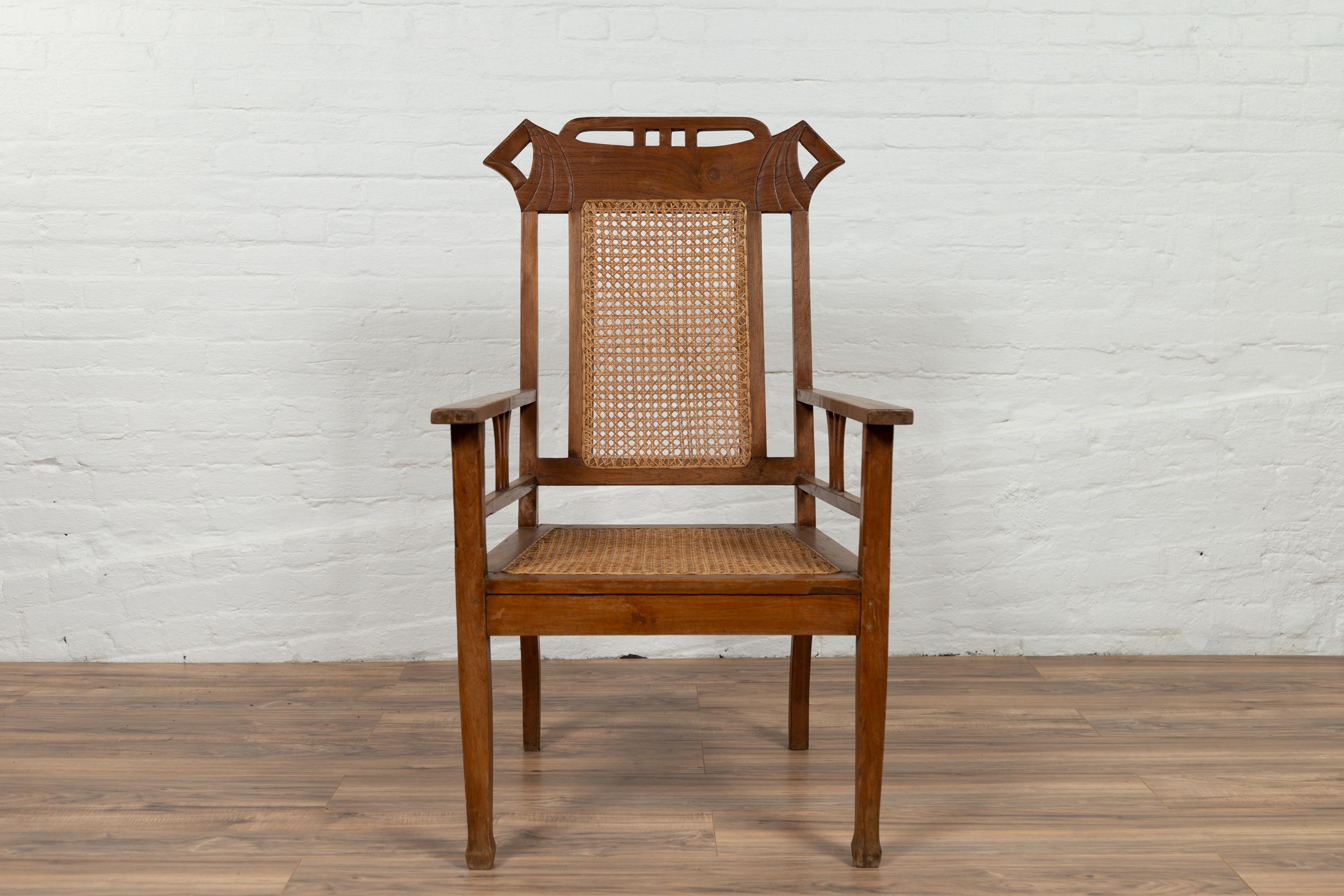 A vintage Indonesian teak wood Dutch Colonial armchair from the mid-20th century, with rattan seat and back. We currently have two available, priced and sold individually. Born in Indonesia during the mid-century period, this Dutch Colonial armchair