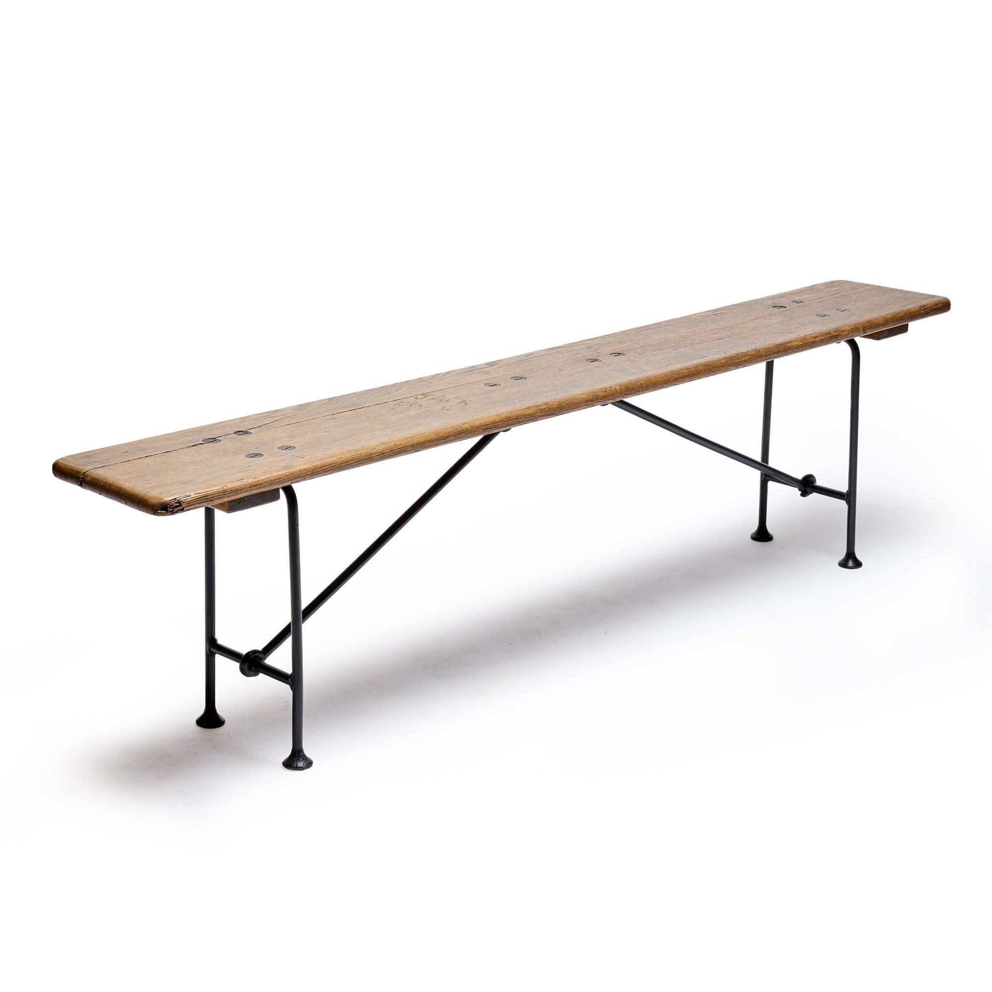 An industrial folding bench with a wood top and wrought iron legs.