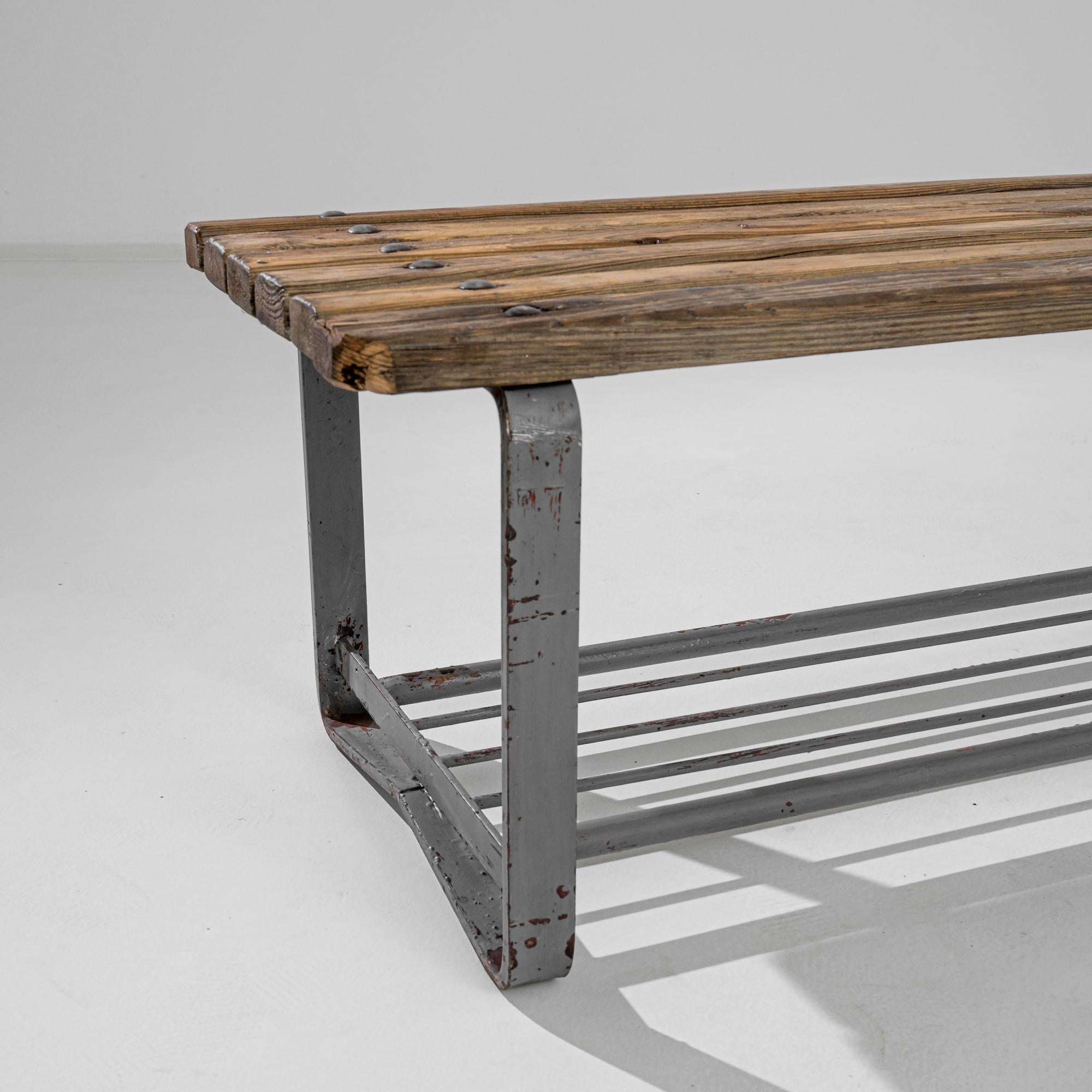 This vintage bench, manufactured in Central Europe, provides a distinctive industrial profile accentuated by the symmetry of the metal base. The slightly weathered gray patina smoothly conjoins the natural finish of the wooden seat screwed to the