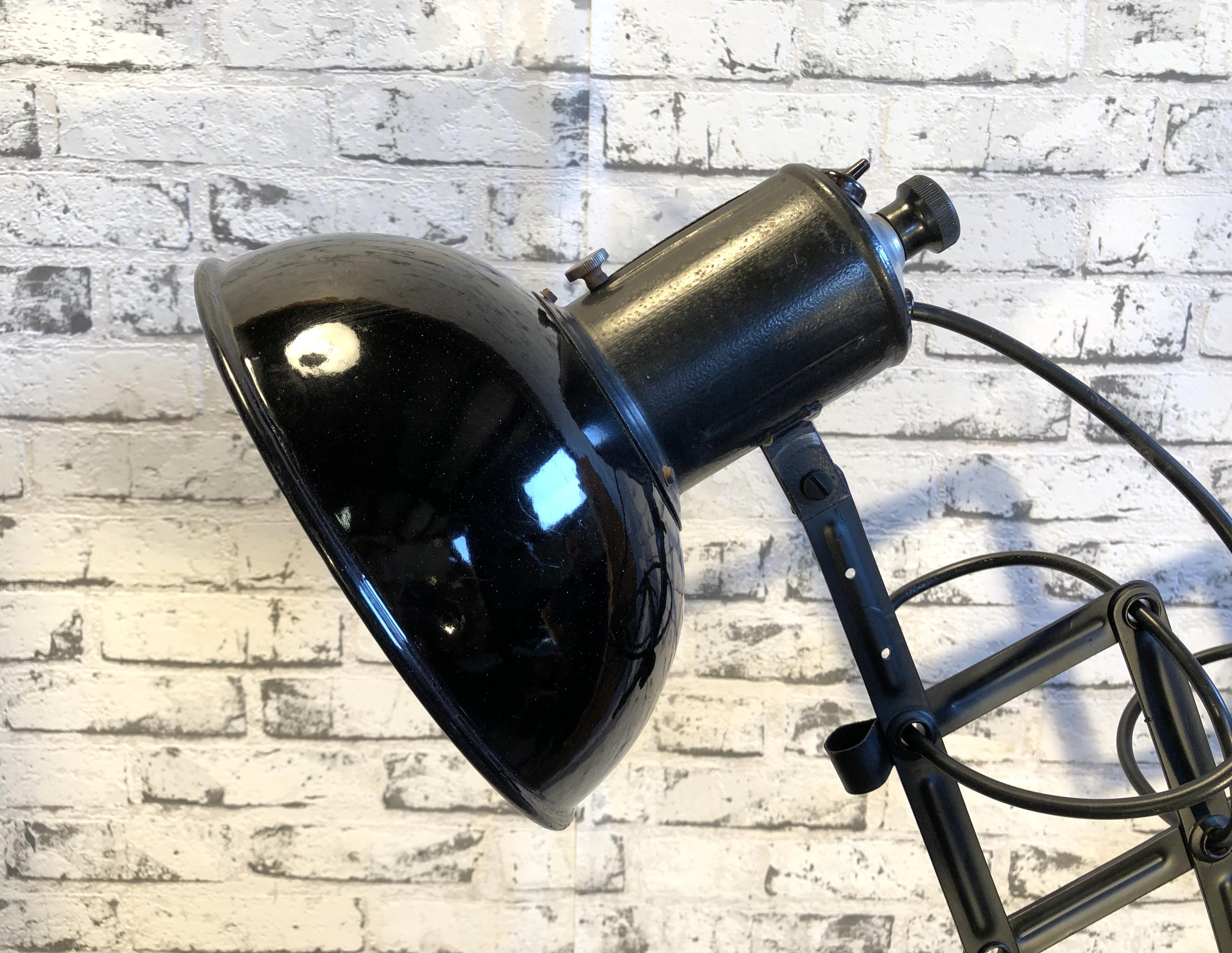This vintage Industrial scissor lamp was produced in former Czechoslovakia during the 1950s. The lamp has a black enamel metal shade, white interior. Black iron scissor arm is extendable and can be turned sideways. The original porcelain socket for