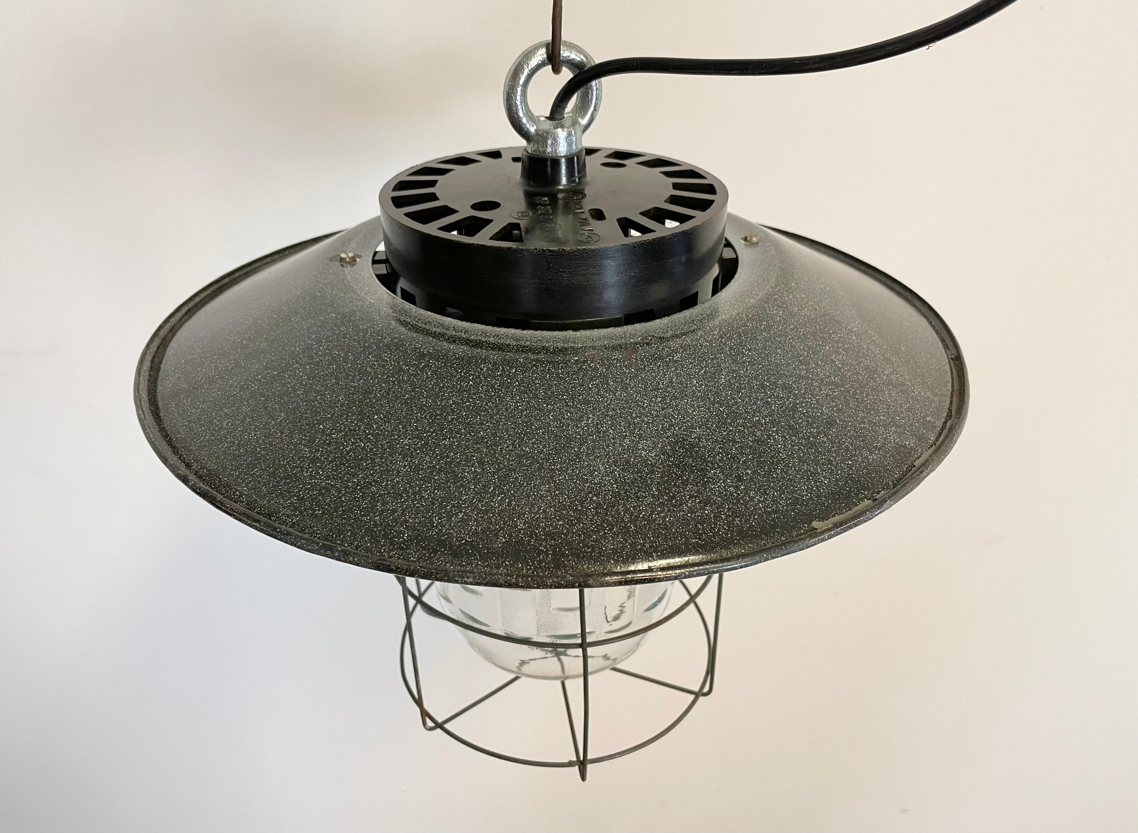 Lampe industrielle vintage fabriquée en ex-Tchécoslovaquie dans les années 1960. Il présente un dessus en bakélite, un abat-jour en émail gris avec un intérieur en émail blanc, une cage en fer et un couvercle en verre. La douille en porcelaine