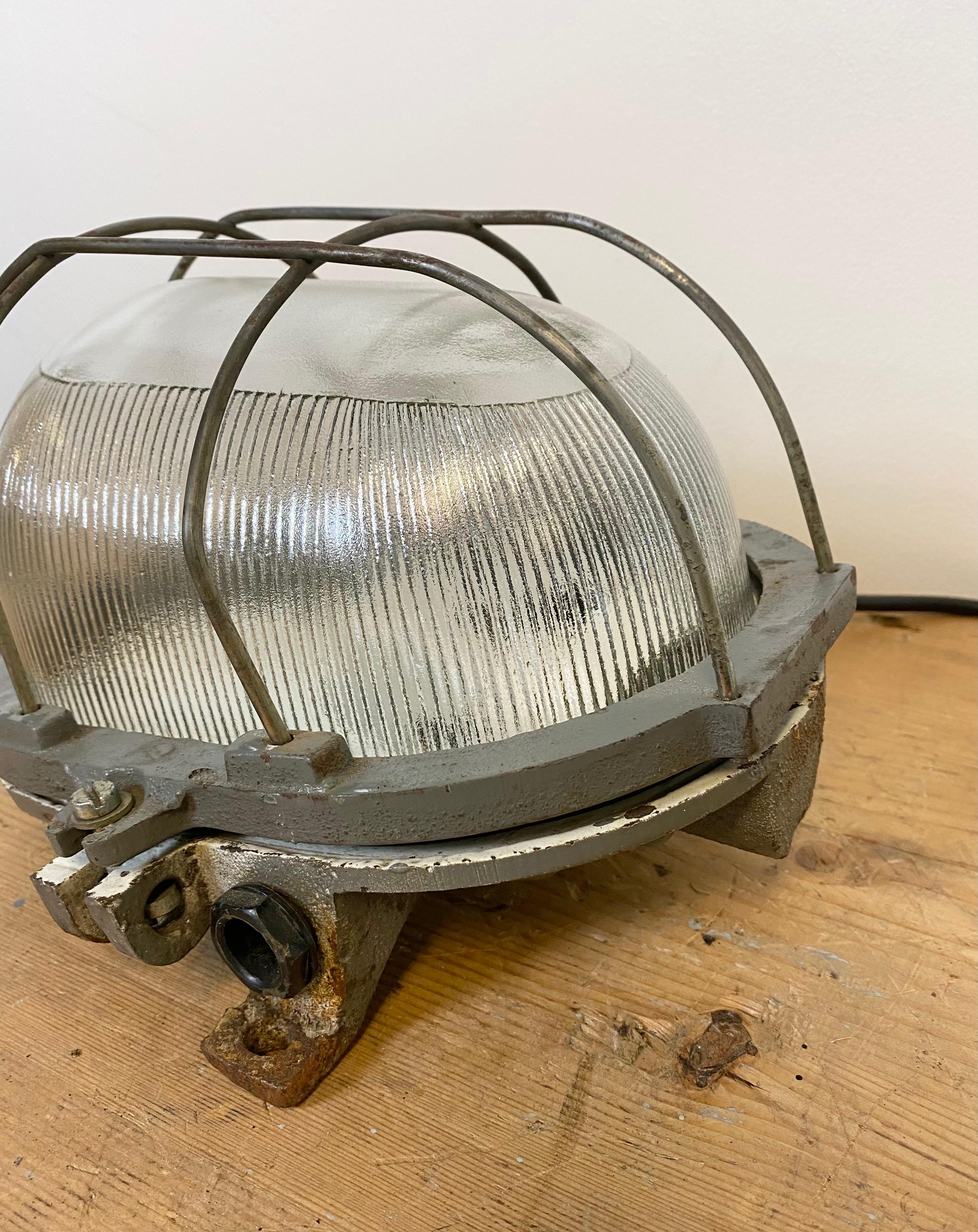 Vintage Industrial wall light from the 1960s. It features cast iron body ,clear striped glass and steel grig. The lamp has a new porcelain socket for E 27 lightbulbs and wire. Good vintage condition. The weight of the lamp is 3.5 kg.