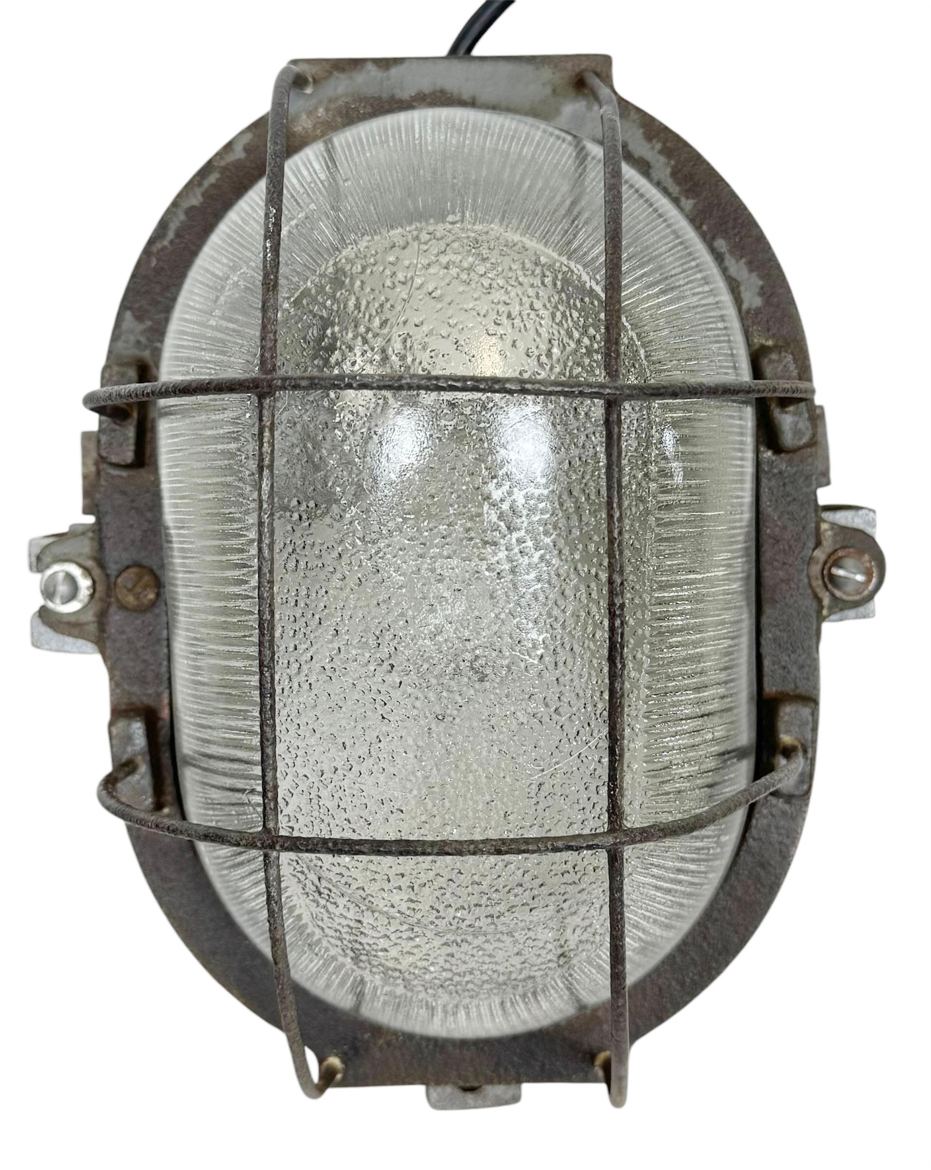 Vintage Industrial wall light made in Poland during the 1960s. It features a cast iron body ,an iron grid and a clear striped glass cover. The socket requires standard E27 / E26 lightbulbs. New wire. The weight of the lamp is 4 kg.