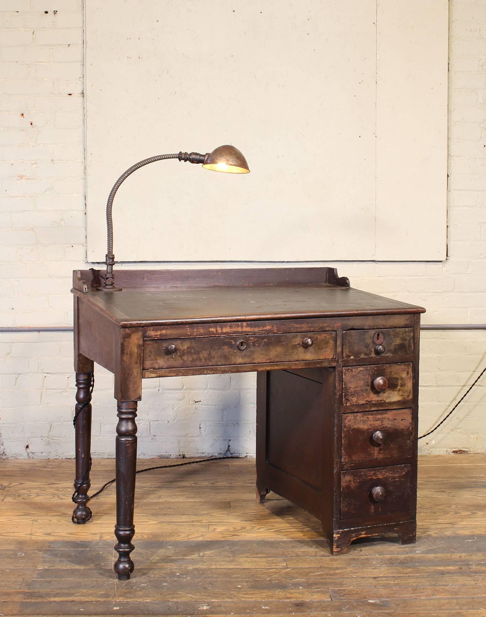 Vintage authentic 1940s clerk's work bench / desk / table. Features an adjustable desk lamp that pre-dates goose-neck. Sloped top with weathered leather insert. Five drawers and turned legs. Desk measures 39 3/4