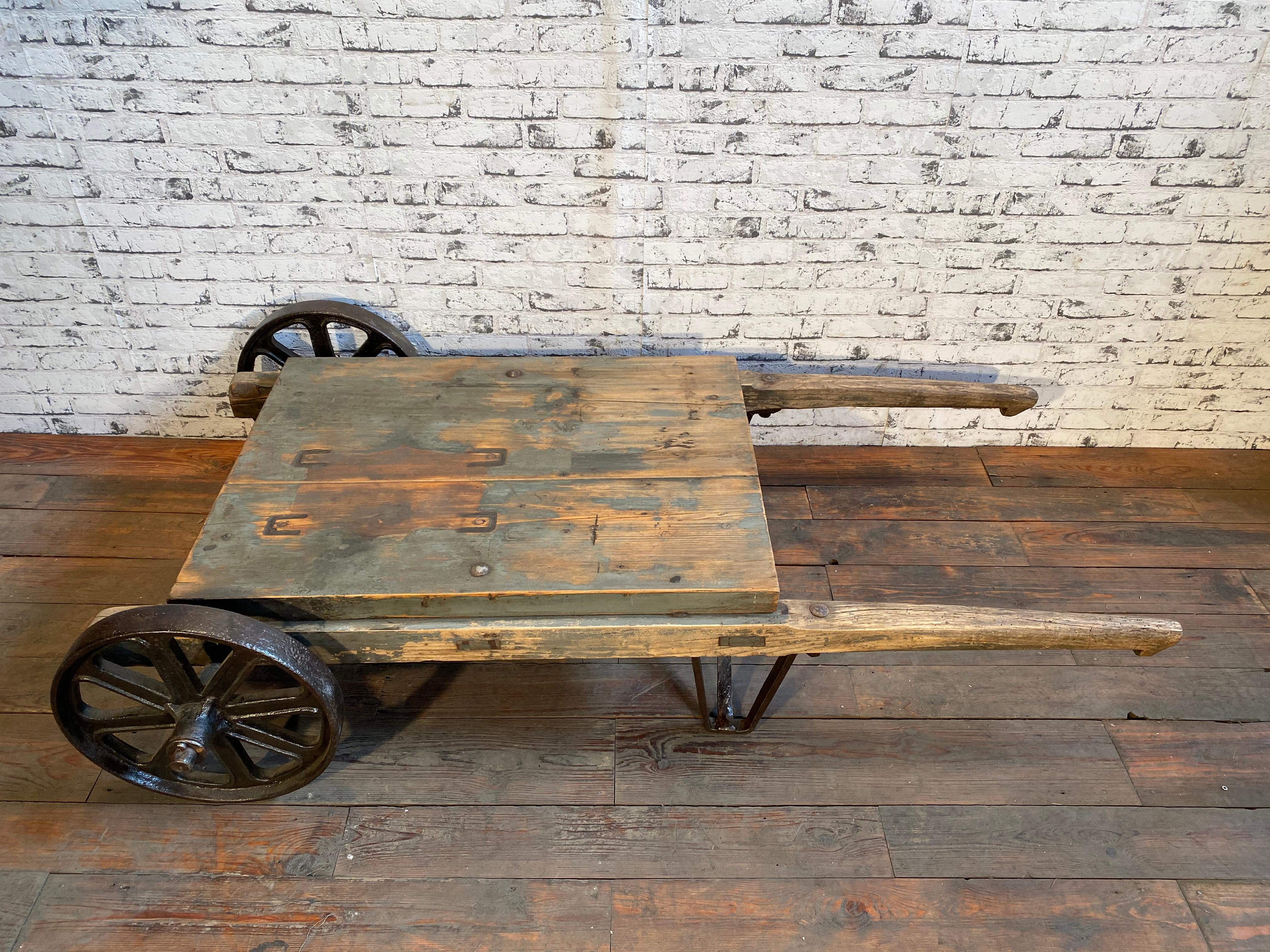 This is an industrial coffee table from the 1950s. It features cast iron legs and a solid old wooden plate with very nice patina. Weight: 55 kg.