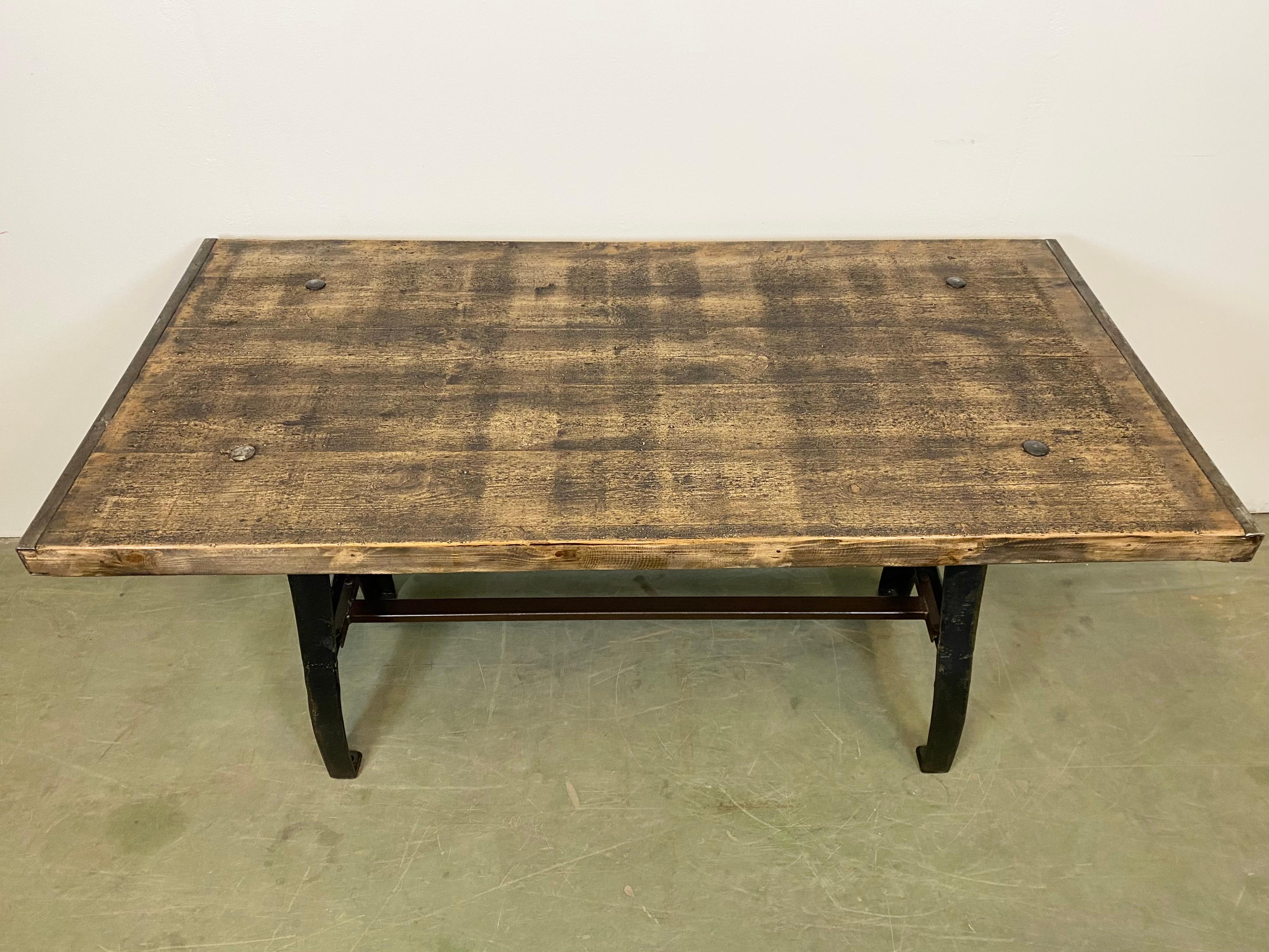 Industrial dining table from 1950s. It features black cast iron legs and a brown solid wooden plate. The weight of the table is 60 kg.