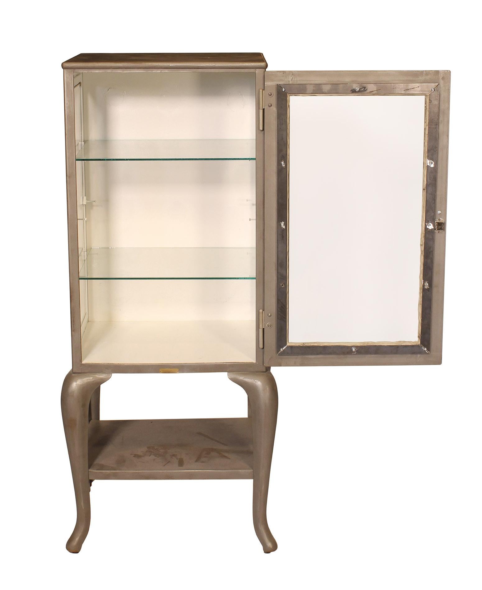 Authentic antique distressed metal and glass doctor's / medical / vitrine cabinet with cabriole legs and two glass shelves. Vintage steel / glass / cast iron storage cabinet is from the 1920s and all original. Cabinet measures 52 1/2