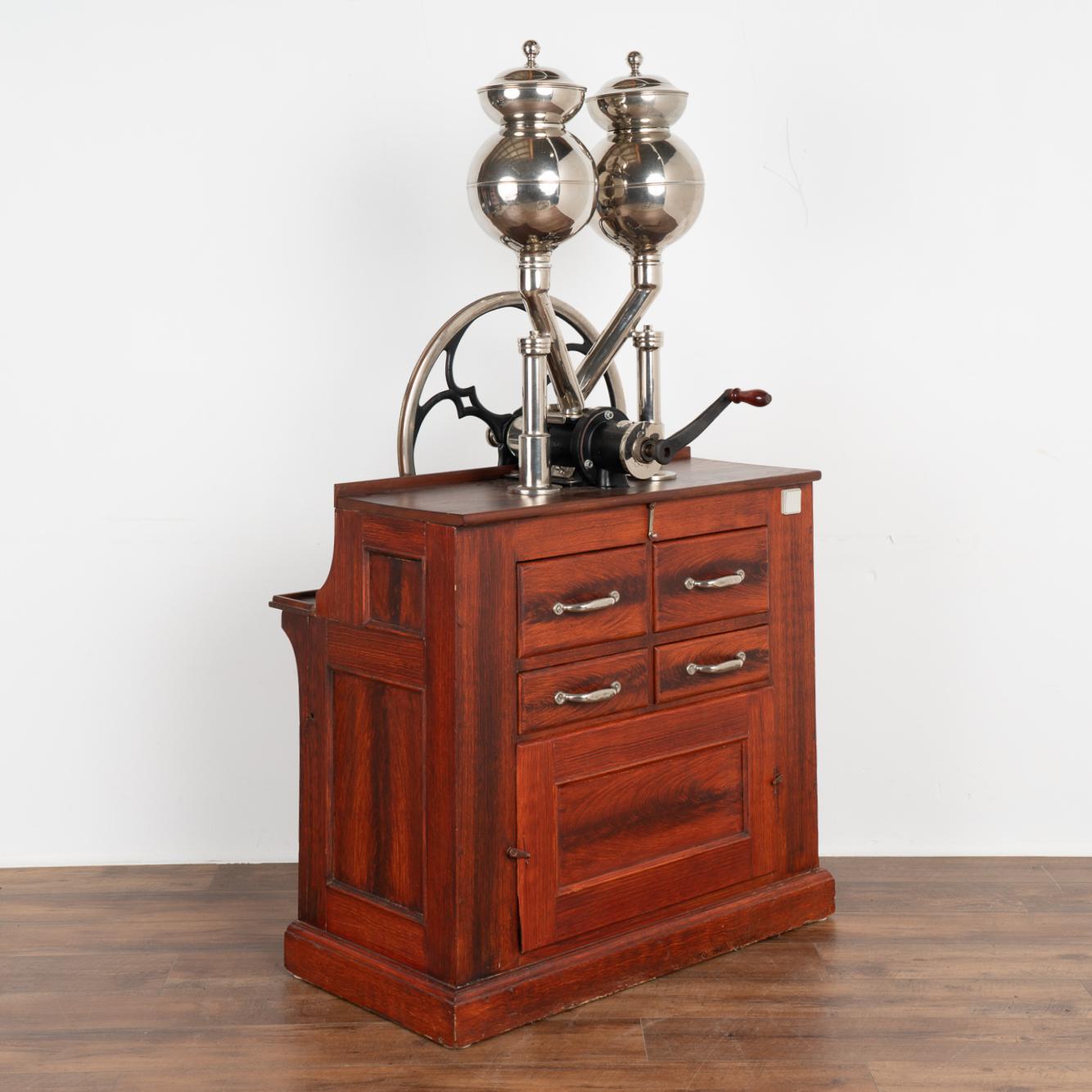 Double coffee mill with motor, two funnels, mill wheel made of iron.
Plaque reads: Frigangs-Kaffemolle; A.Jørgensens & Co. (of Copenhagen, Denmark).
Lower part of red painted wood with metal lined drawers to capture coffee grounds. 
Sold in