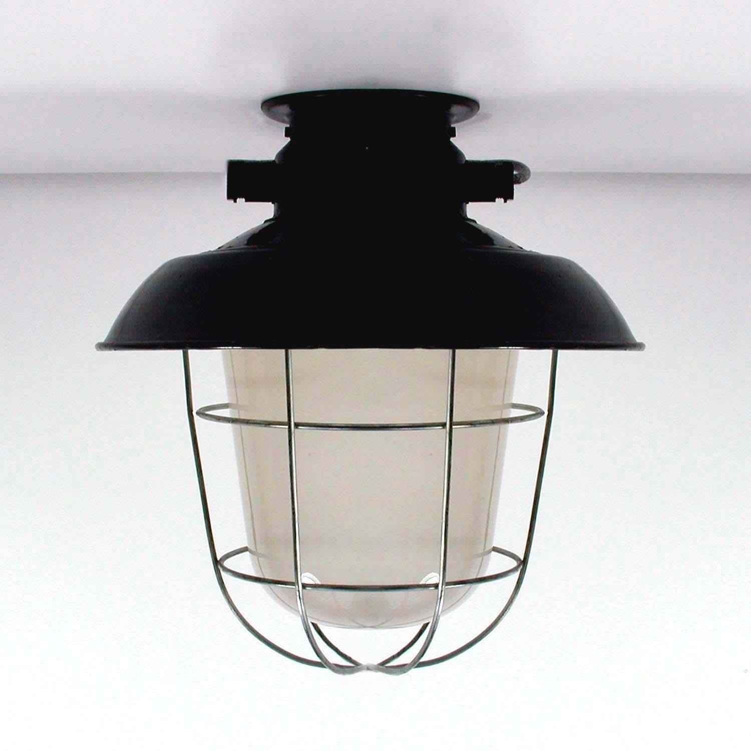 This vintage industrial flush mount was made in Germany in the 1940s to 1950s. The lamp features a black enamel lamp shade and a milk glass cylinder to protect the bulb. The lamp can be used as a ceiling light as well as a desk or table lamp.
   