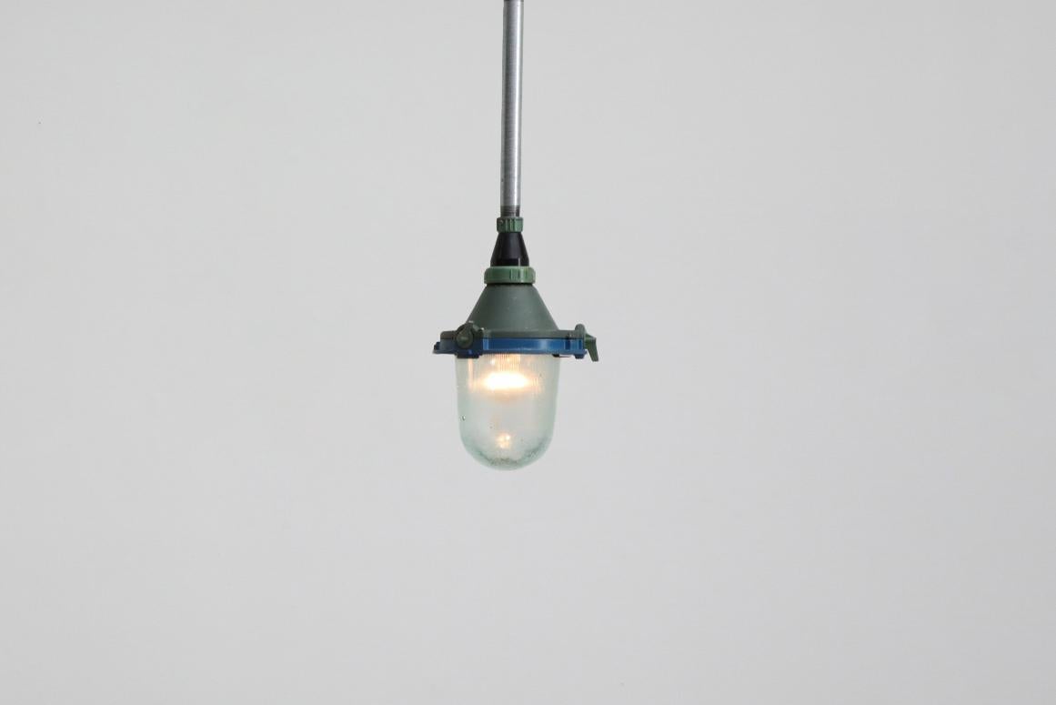 Vintage industrial hanging factory lamps with enameled metal casing, glass shades and steel pipe stems. This one has a moss green casing with a blue collar and seafoam green and black hardware. In original condition with visible wear including
