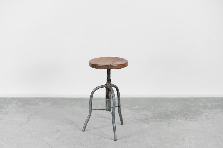 This swivel stool was produced in Poland during the 1950s. The round wooden seat is mounted on a solid metal screw. The massive three legs are connected to each other. The seat can be adjusted from 49 cm to 68 cm. Ideally suited to industrial or