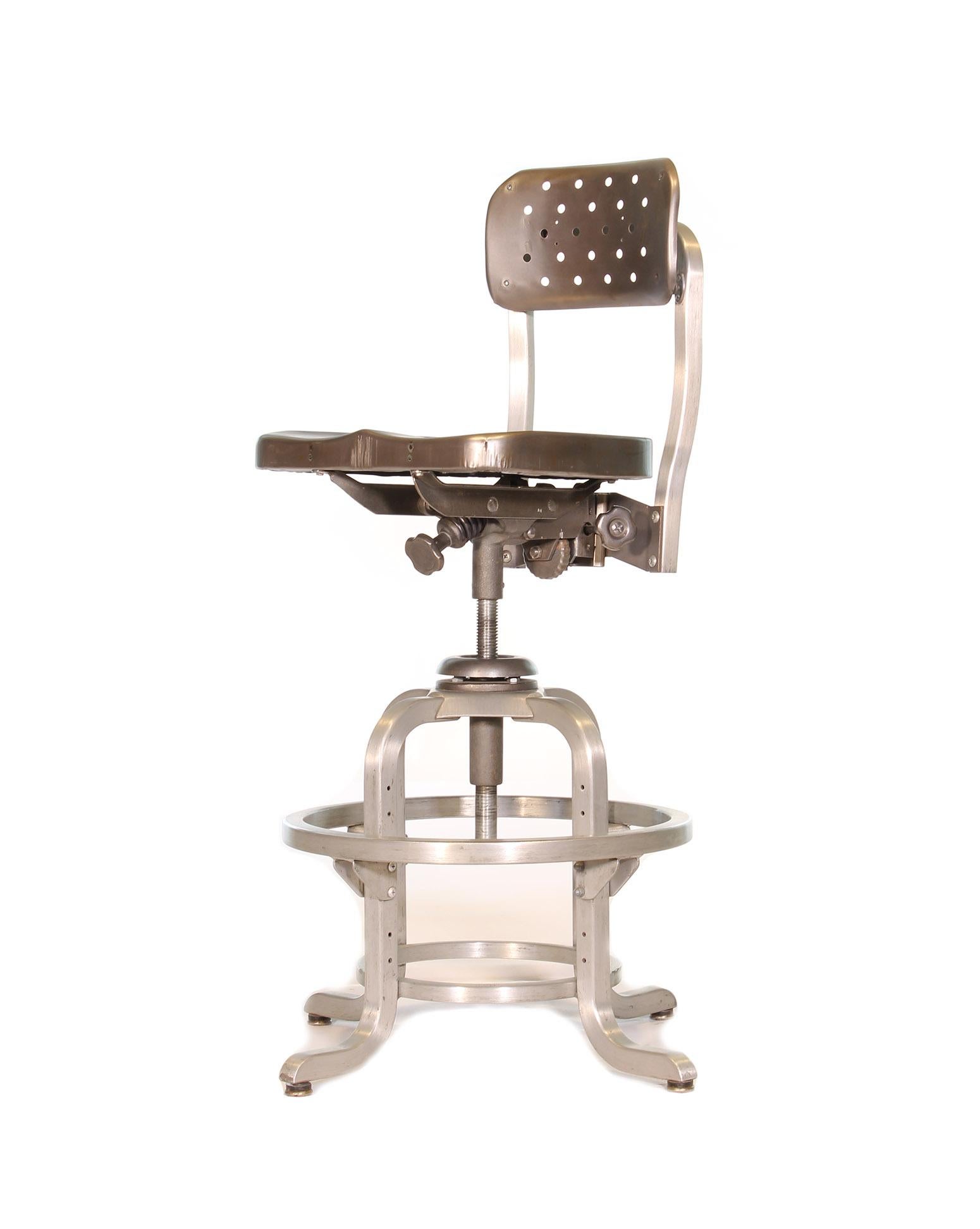 Authentic aluminum adjustable drafting stool by GoodForm. Features perforated seat and pivoting back rest. Back rest height, angle and tension are adjustable. Foot ring height and seat height are also adjustable. Foot rest measures 18 3/8