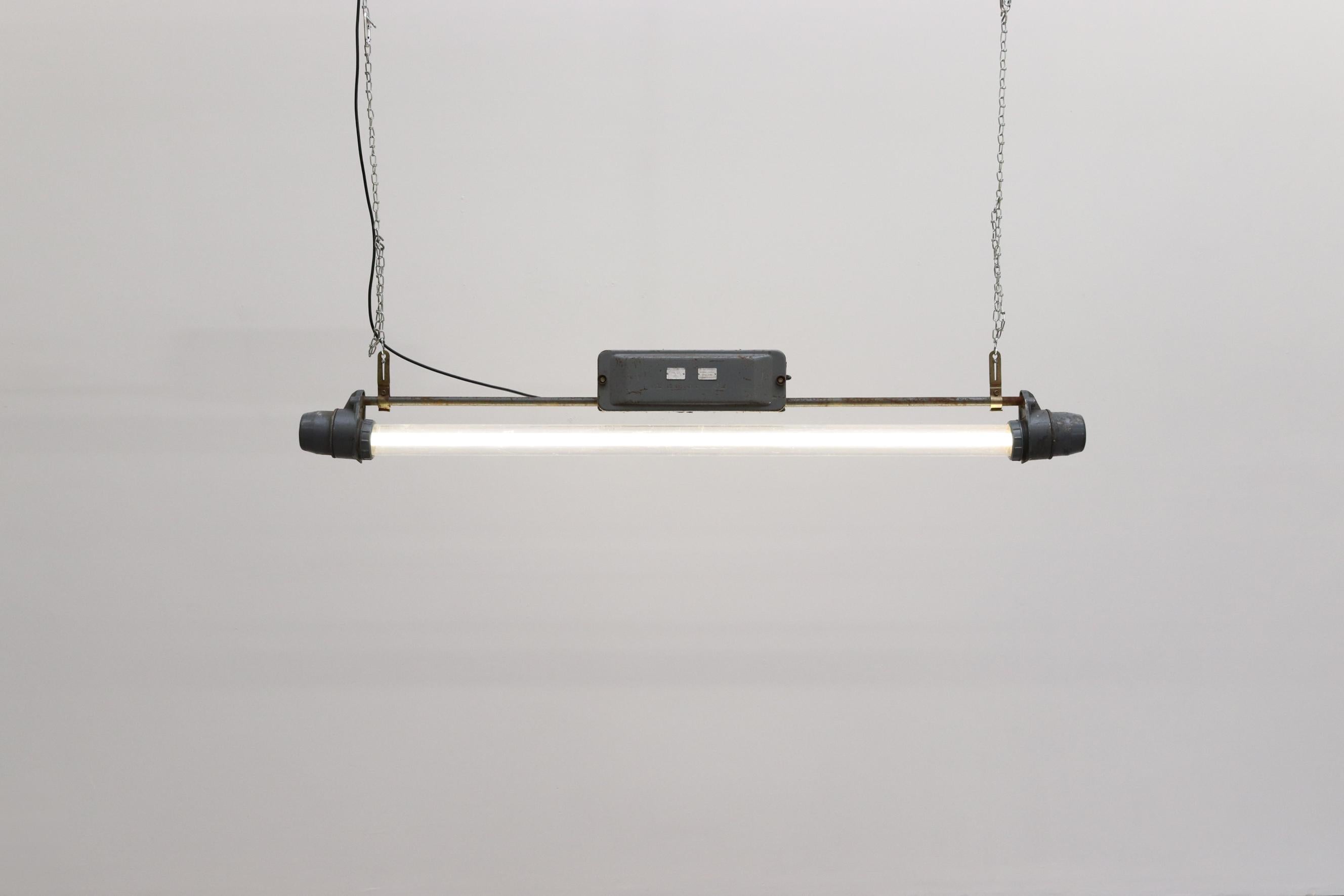 Vintage industrial hanging fluorescent tube light. Plexiglass encased fluorescent tube In original condition with visible wear and heavy patina. Wear is consistent with its age and use.