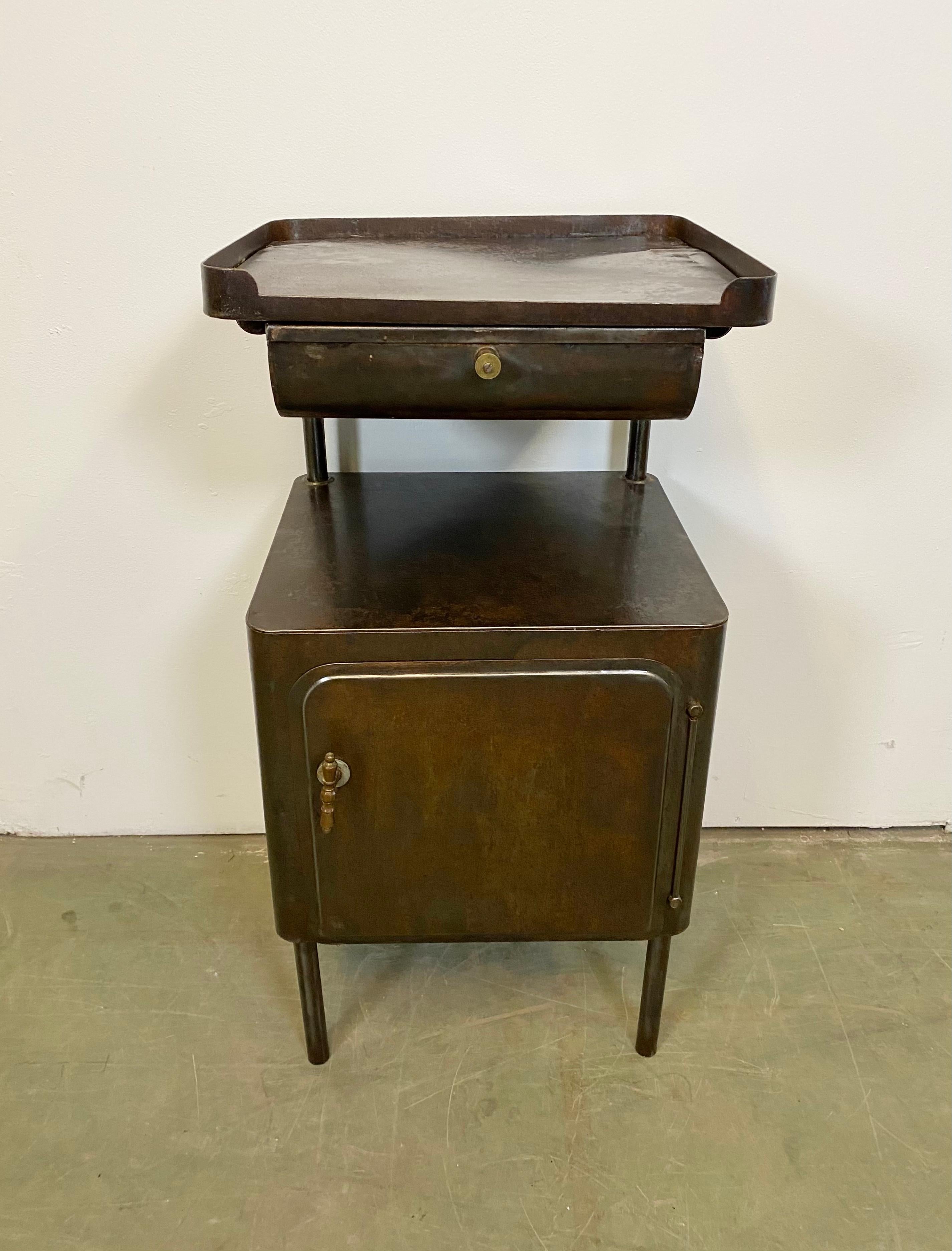 - Industrial, brushed, metal, 2-tier, hospital nightstand cabinet.
- Made during the 1950s.
- It features a storage on the bottom and a drawer on top.
- Brass buttons
- The weight of the nightstand is 11 kg.