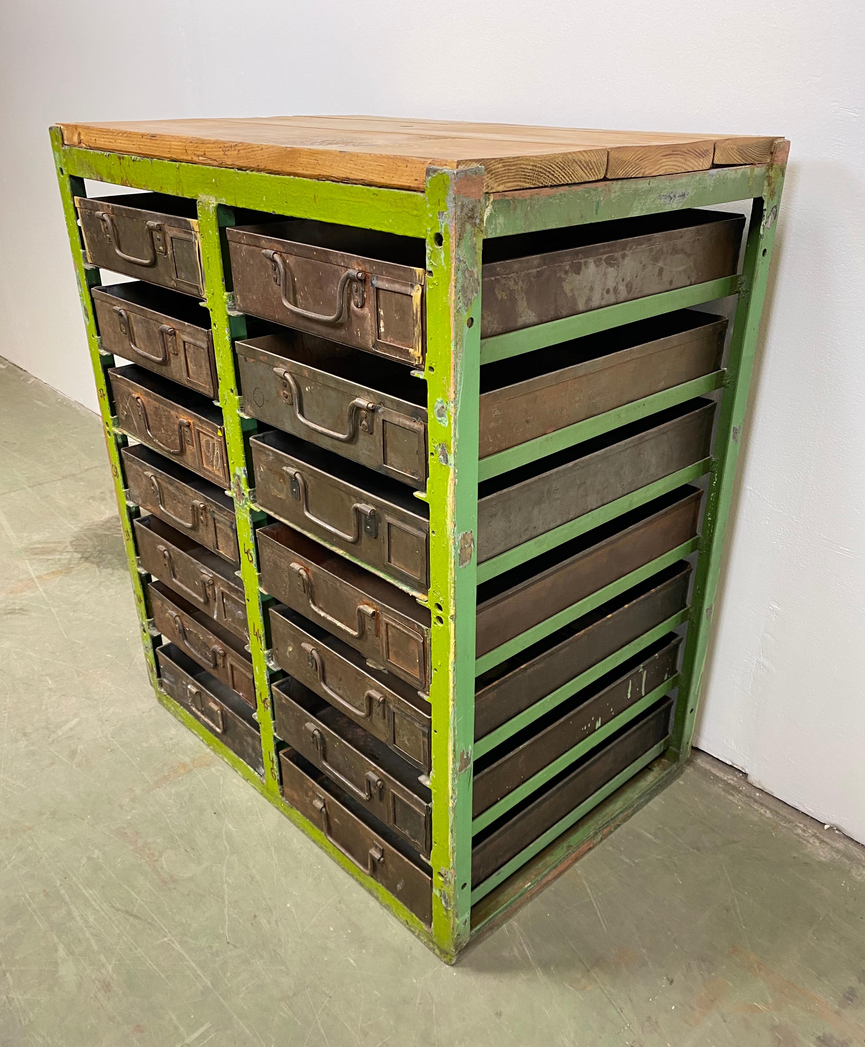 This vintage industrial iron chest of drawers was made during the 1950s. It features green iron construction, old wooden top and 14 metal drawers.

Additional dimensions:
- Drawer dimensions Width 8 cm, depth 44 cm, height 8 cm
- Weight: 57 kg.