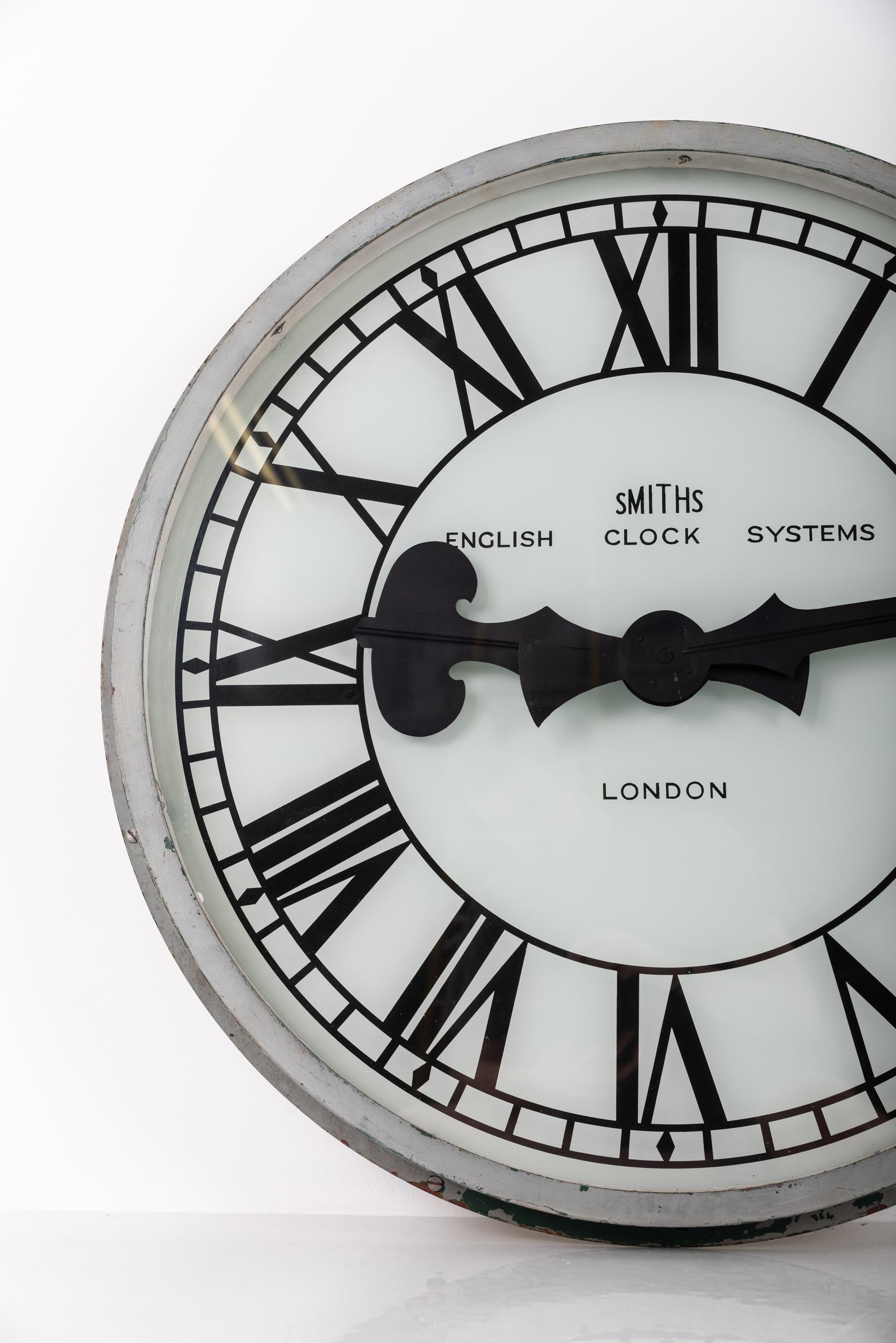 Exceptional example of a large illuminated wall clock manufactured by Smiths English Clock Systems. c.1930

Heavy gauge steel casing in old grey paint - presumably once flush mounted into an opening - now has a custom mount made. The dial is made of
