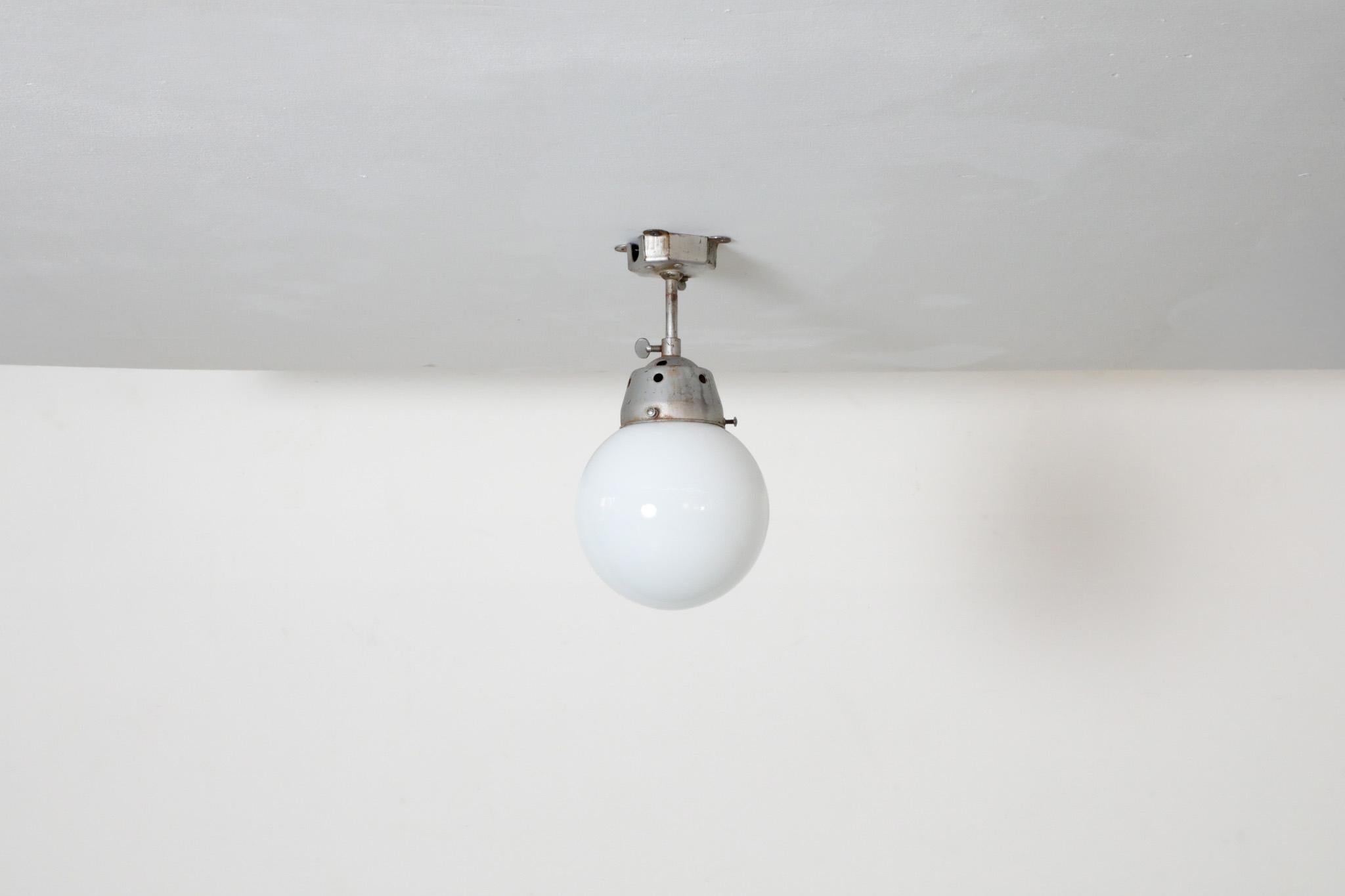 Vintage industrial ceiling or wall light with opaline glass globe and raw metal mounting. Height adjustable by twisting thumbscrew, as well as the ability to tilt back and forth. Shade is fastened by side screws. In original condition with some