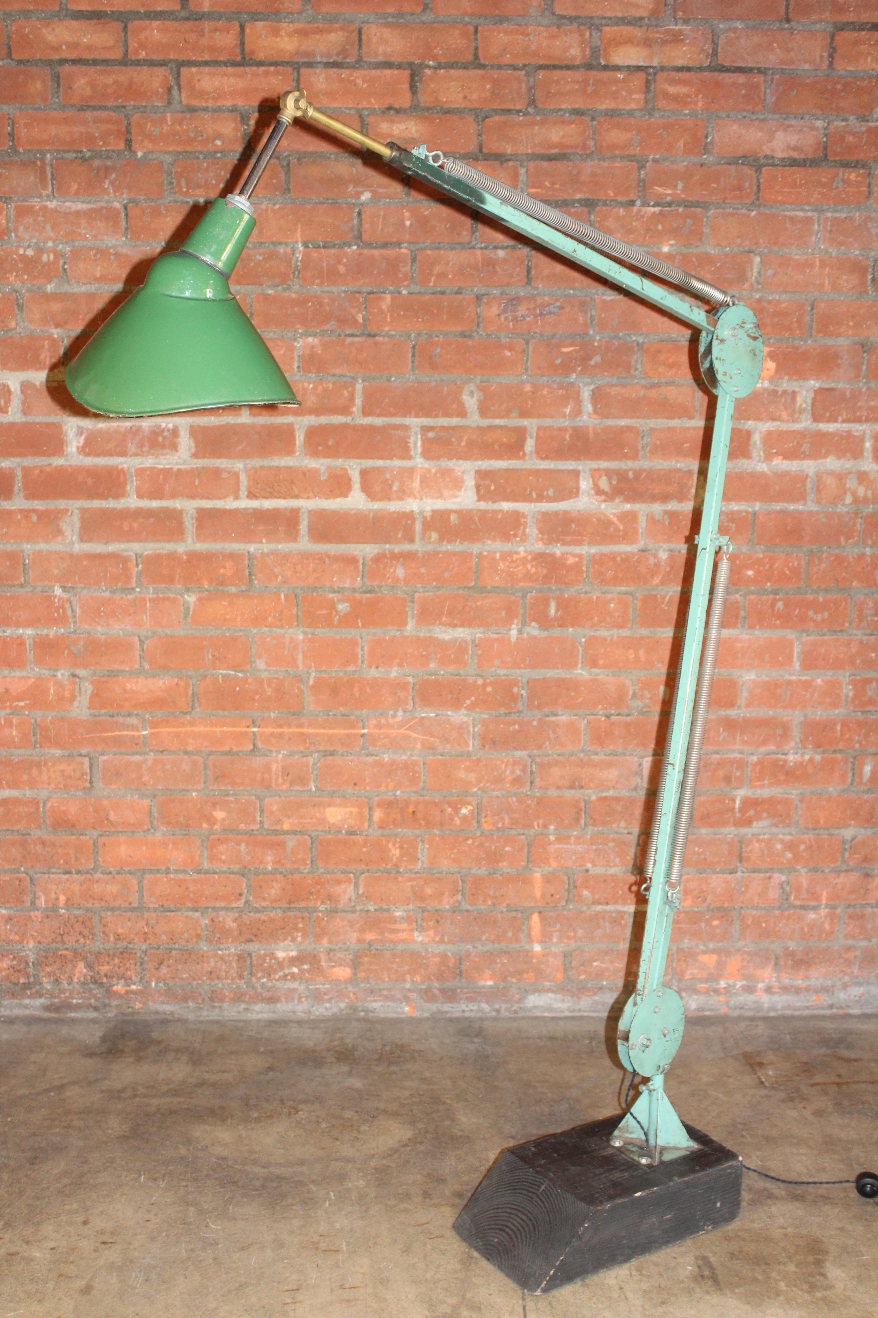A vintage industrial pivoting and adjustable floor lamp. Newly rewired. Features a wooden base. The painted finish shows patina.