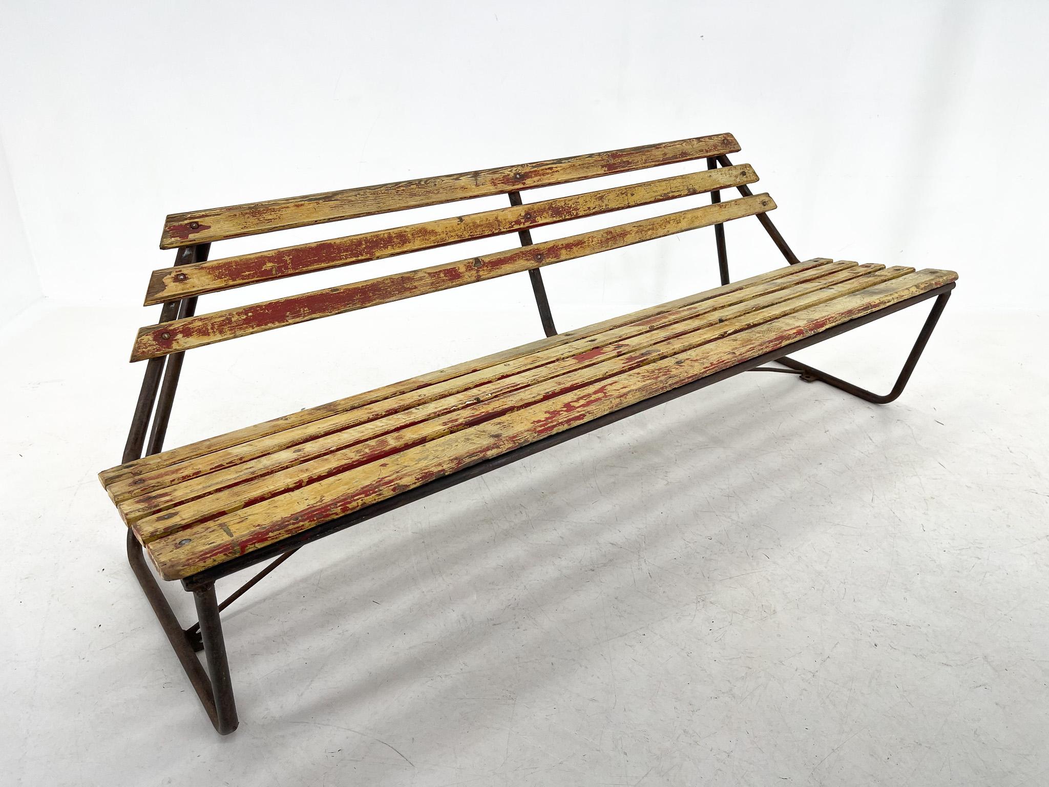 Vintage wooden bench with atypical shape. The metal construction is very stable. The wooden slats have the original paint on them and the influence of the years has created a beautiful yellow-red patina.