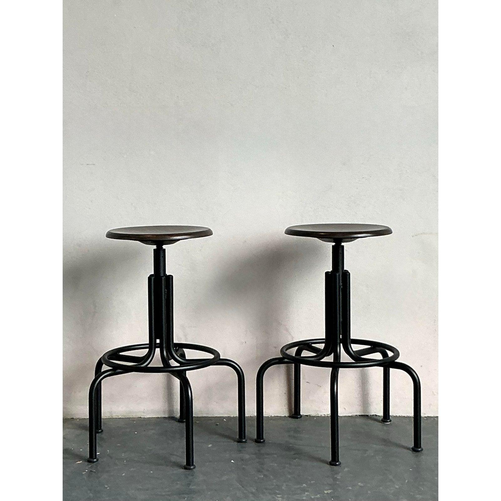 Embrace the rugged charm and versatile functionality of this pair of vintage industrial swivel stools. Crafted with a sturdy black metal base featuring gracefully curved legs and a circular footrest, these stools exude a timeless factory-chic