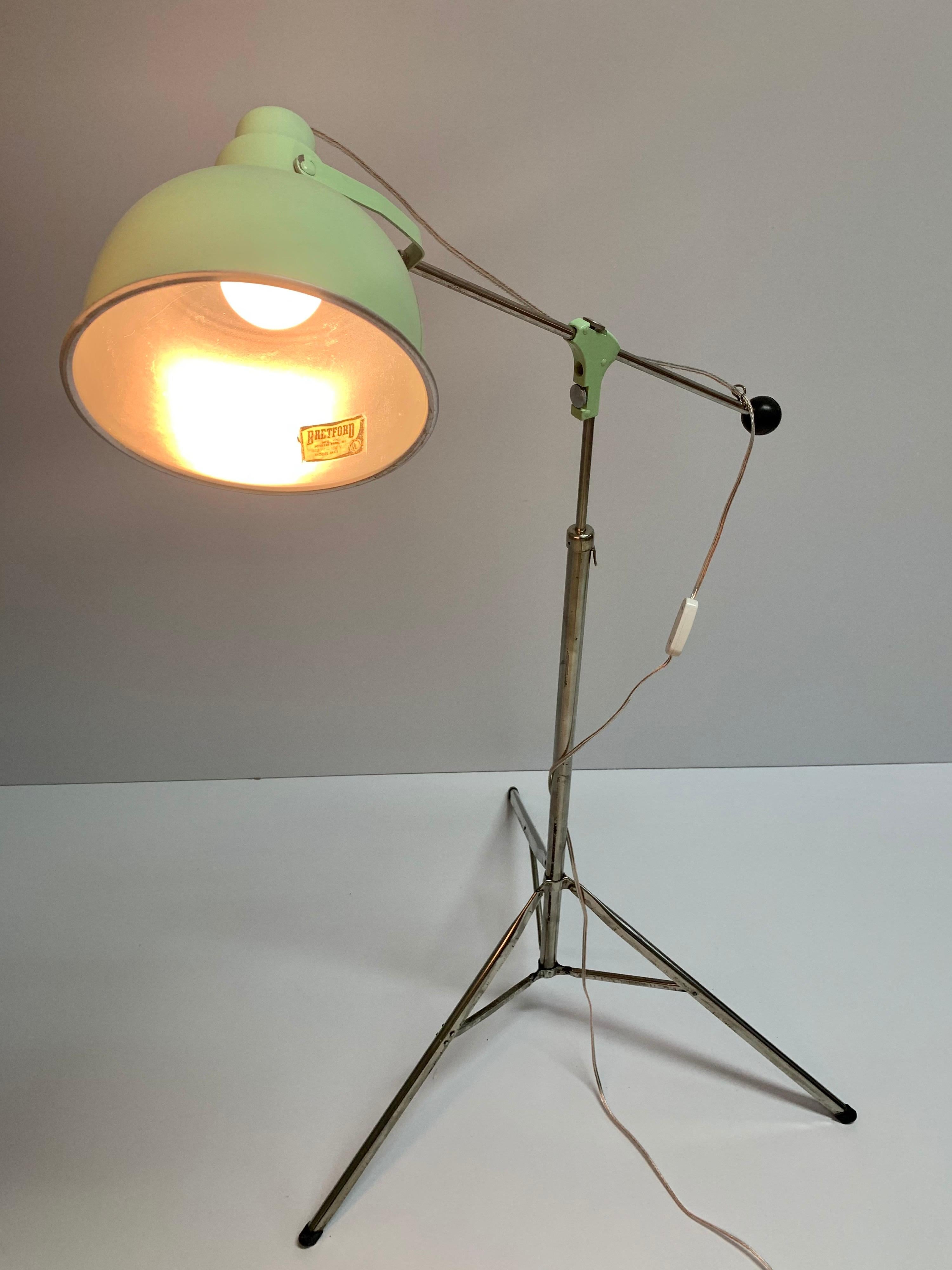 Vintage industrial telescoping adjustable floor lamp with a tripod base by Bretford Manufacturing Company of Franklin Park, Illinois, labeled “Model MJ-1.” The shade of the lamp can be tilted to adjust the angle of the light, and the arm slides back