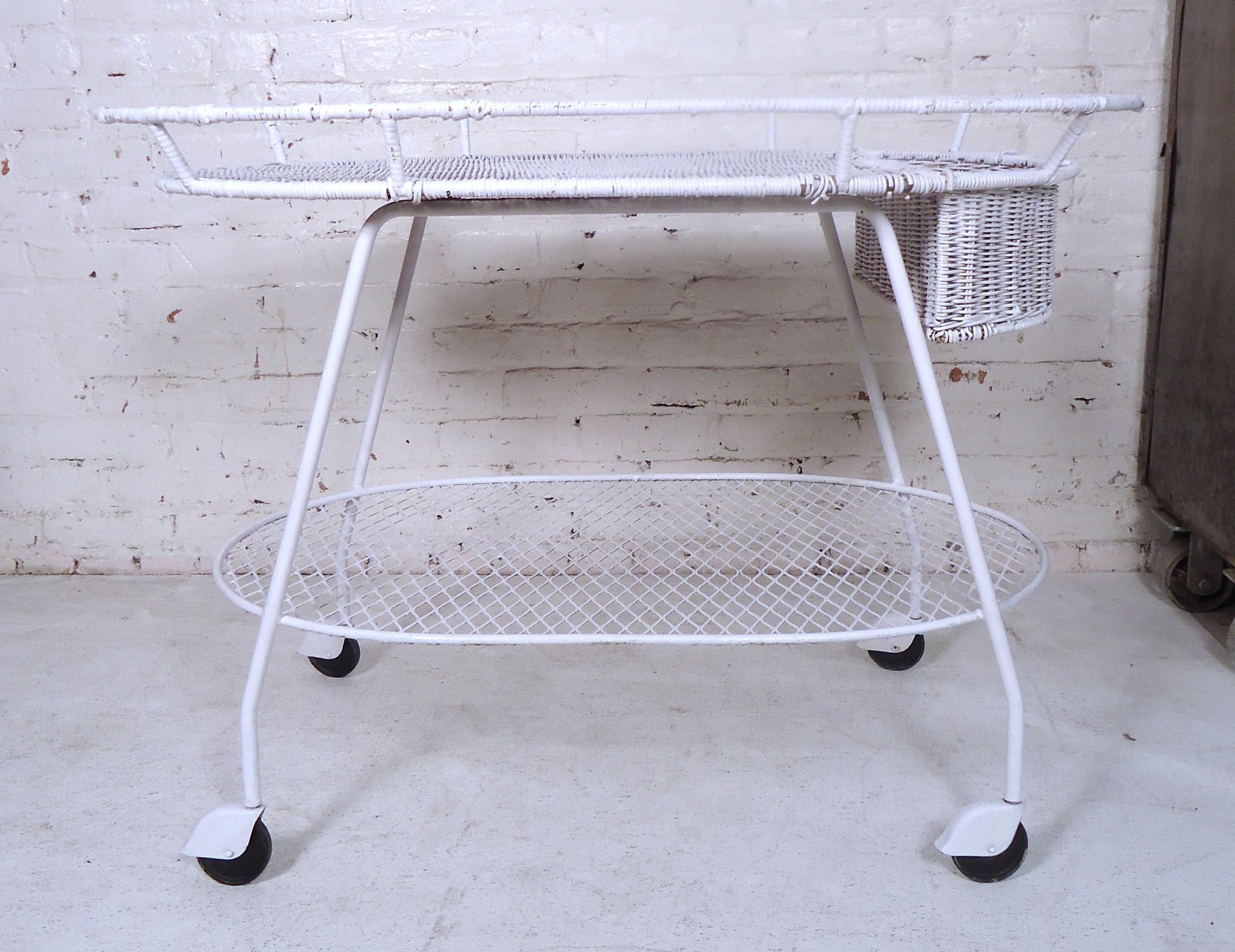 Unique vintage modern two-tier tea cart featuring a painted white metal frame, wicker top, and set of four wheels.
 
