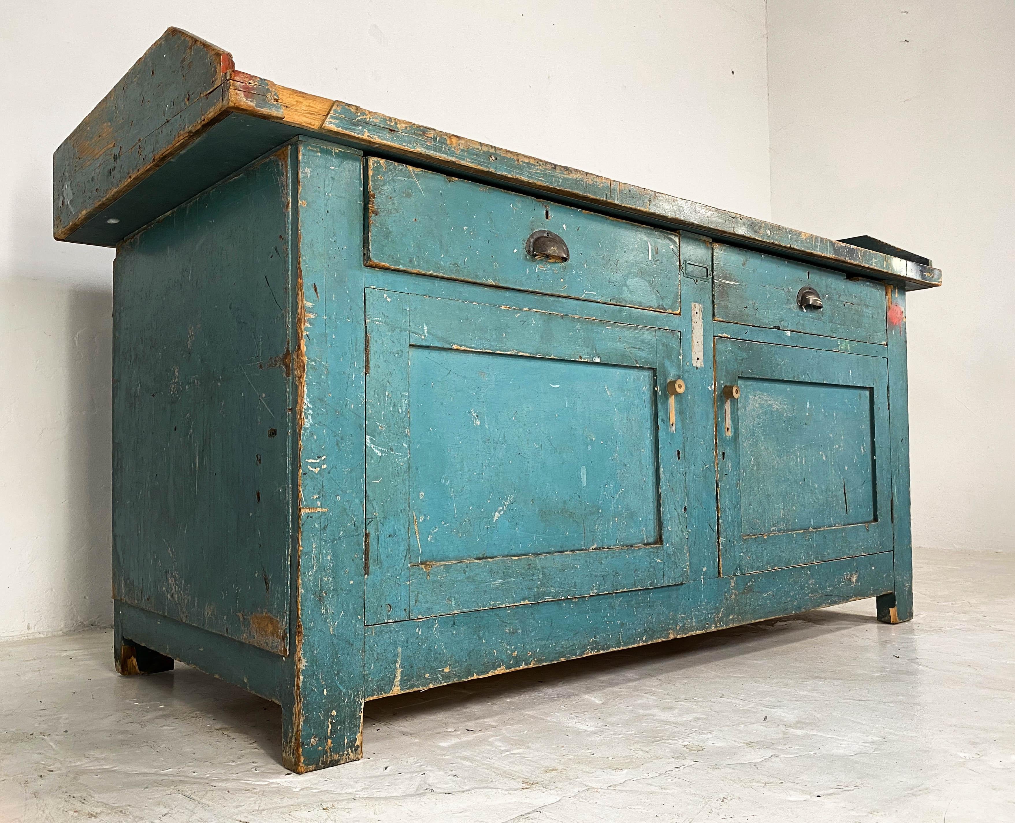 Gorgeous turquoise blue workbench which originated from a bicycle repair shop in Nottingham, England; a city famous for manufacturing Raleigh bicycles.
It has all original plywood panels, two drawers with brass cup handles and plenty of storage in
