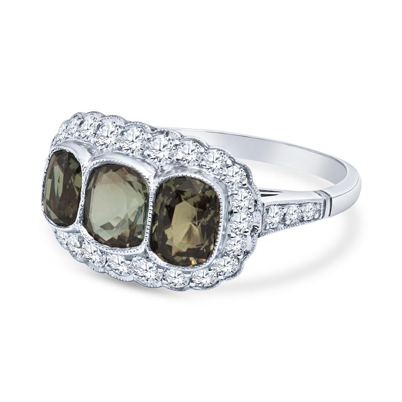 This vintage art deco inspired ring features three natural cushion cut alexandrite's weighing 2.35 carats accented by 0.60 carat total weight in round diamonds set in platinum. The ring features delicate milgrain detailing. It is a size 7 but can be