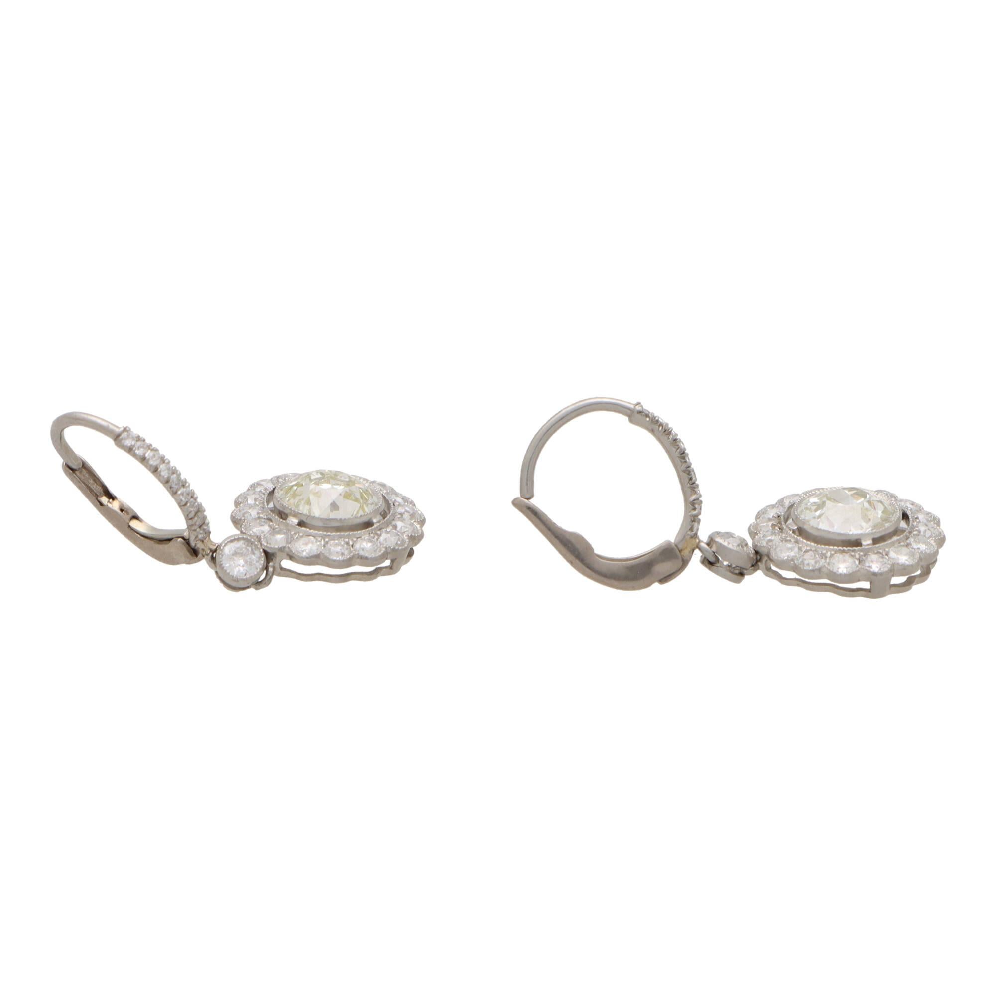 A beautiful pair of vintage inspired round diamond cluster drop earrings set in platinum.

Each earring is composed of a single 1.25 carat old  European cut central diamond which is rubover set with a milled edge to the centre of a halo of  smaller