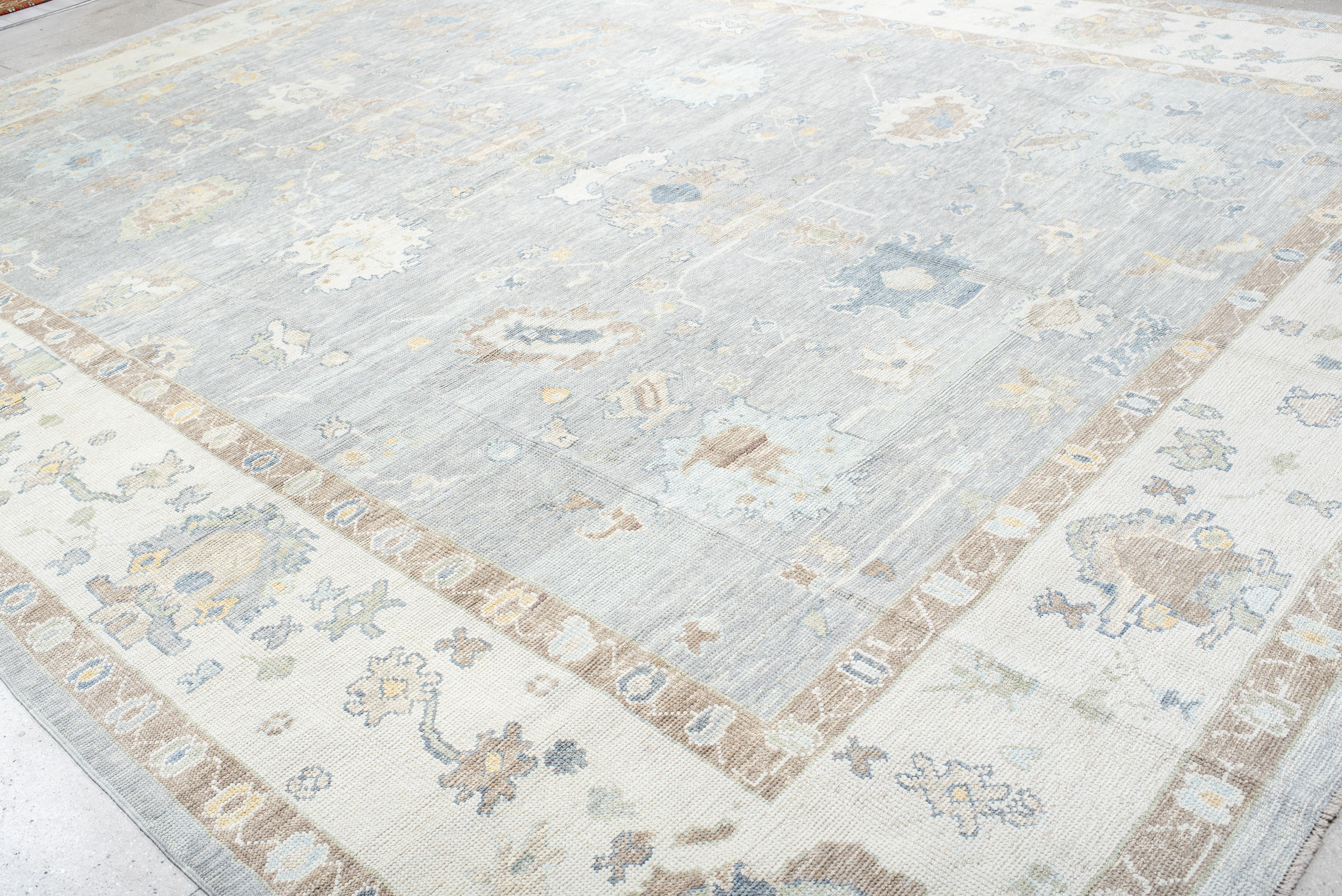 A grand yet understated statement, this Oushak rug is a masterclass in balance and restraint. The expansive field is adorned with softly rendered botanical and tribal motifs, thoughtfully spaced to create an airy, open composition. A delicate border