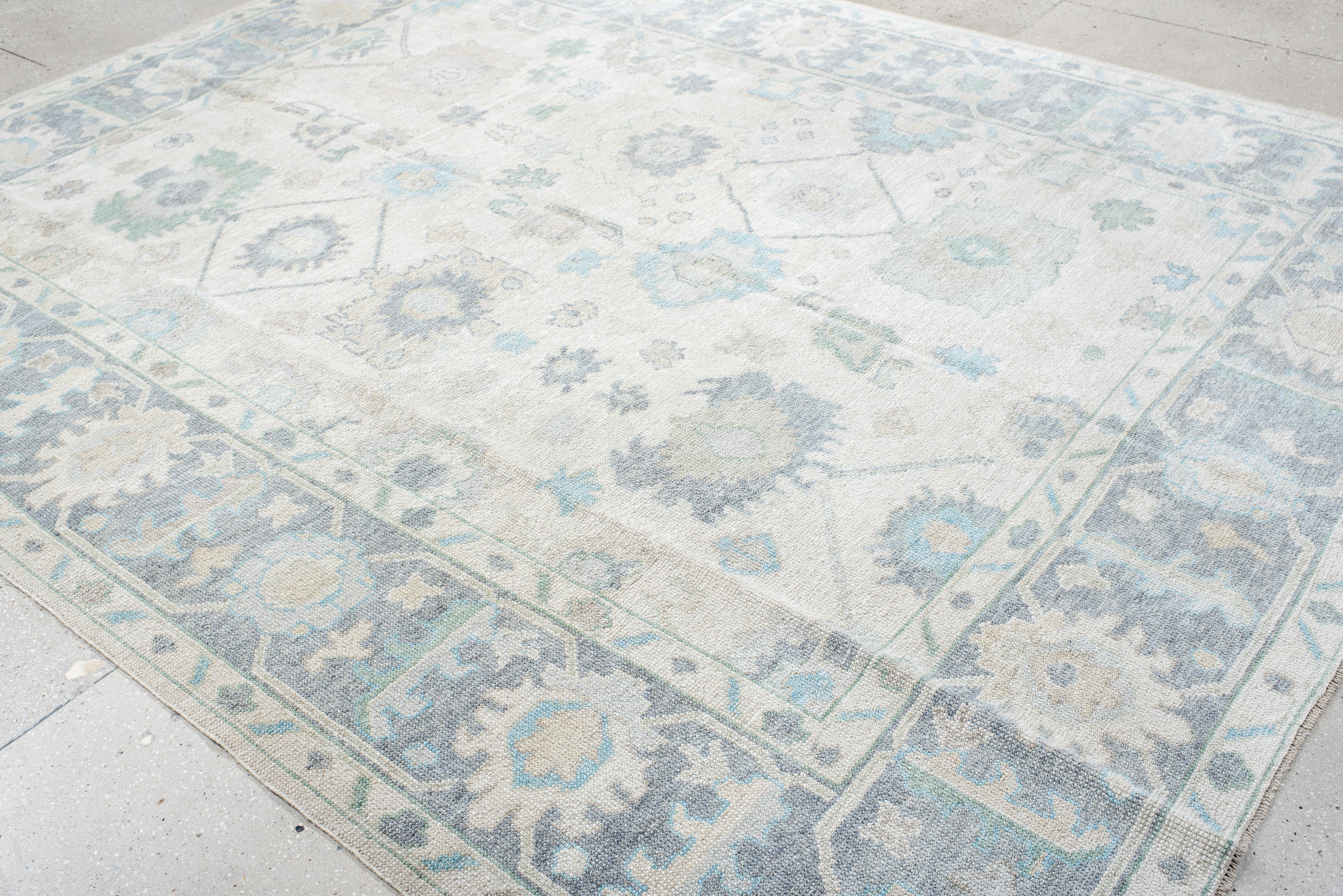This handwoven Oushak rug embodies a soft, ethereal presence with its delicately faded palette. A harmonious blend of pale ivory, muted blues, and subtle hints of sage green creates an airy, tranquil foundation. The intricate botanical and geometric