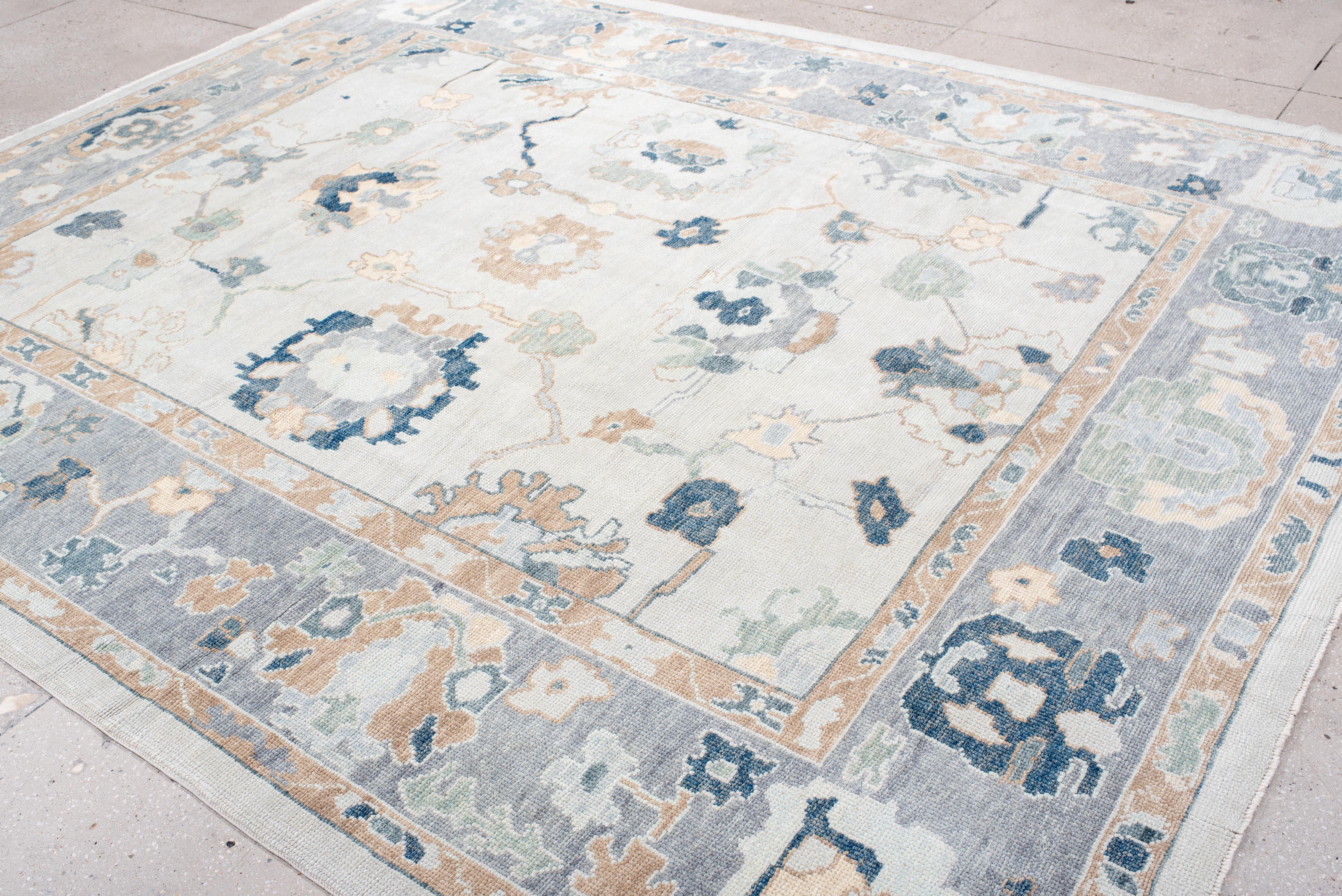 A thoughtfully woven Oushak rug with a beautifully aged character, this piece features a serene palette of soft greys, warm beige, and muted blues with delicate hints of sage. The intricate botanical motifs and structured border add a sense of