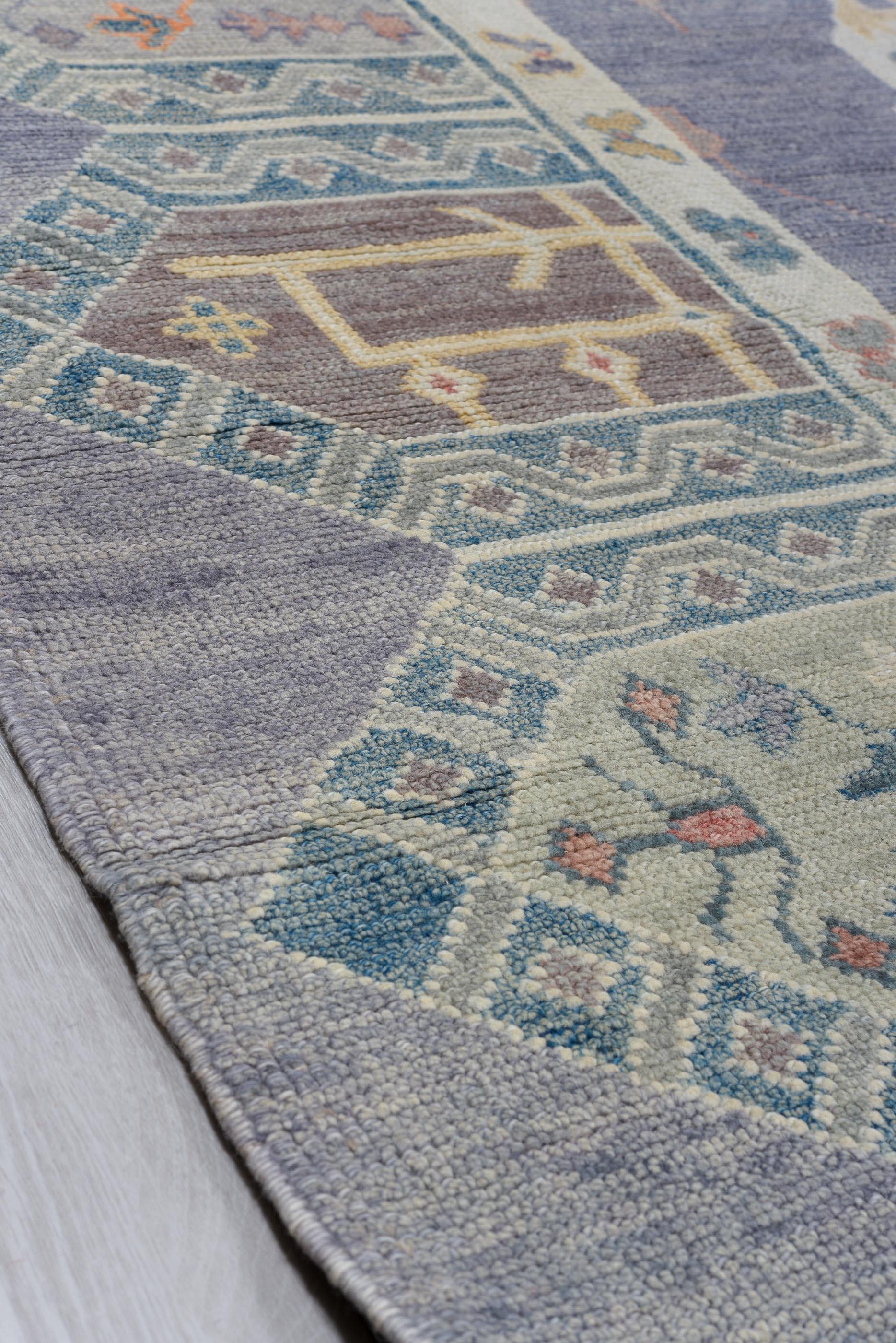 A tapestry of tradition and modernity, this Oushak rug is defined by its striking latticework of elongated diamond motifs, each enclosing delicate tribal symbols and organic flourishes. The structured repetition creates a rhythmic flow, while the