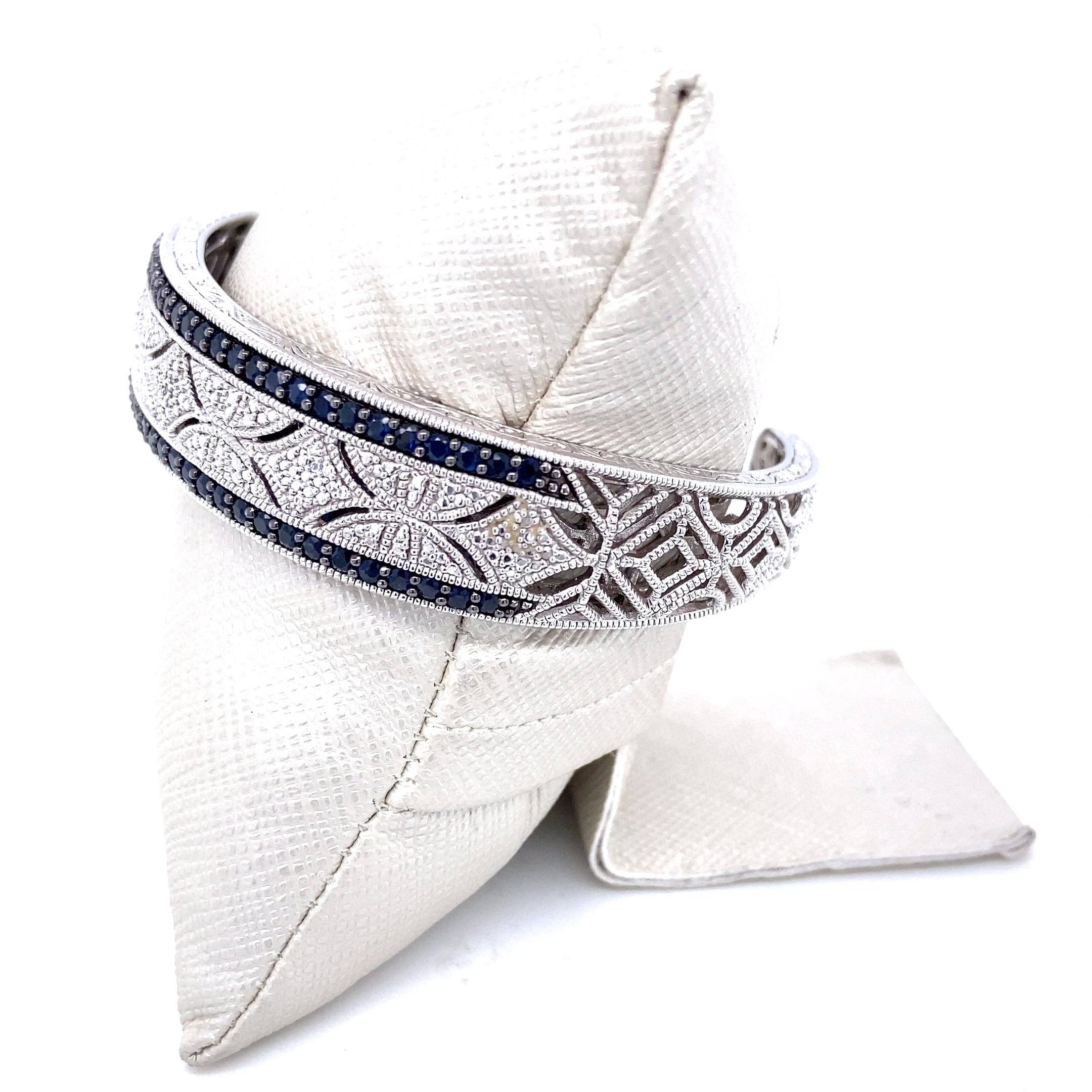 This vintage inspired sterling silver hinged bangle bracelet is bejeweled by 0.10 carat total weight of single cut diamonds that are J color and I2 - I3 clarity which are flanked on each side by deep navy blue round sapphires which have an
