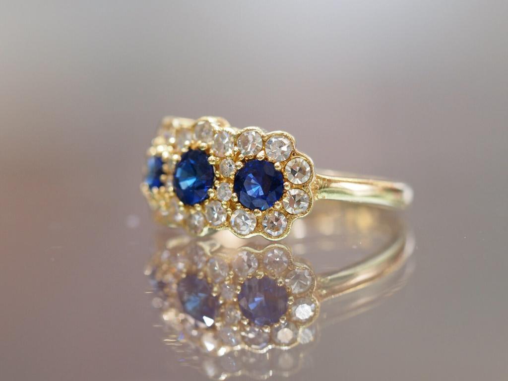 Beautiful three stone natural blue sapphire fashion ring with a modern vintage touch is  accented with single cut round diamonds set in a “flowery” style halo around each sapphire with a light milgrain edge. 14k Yellow gold. Size 5.75 (sizeable)