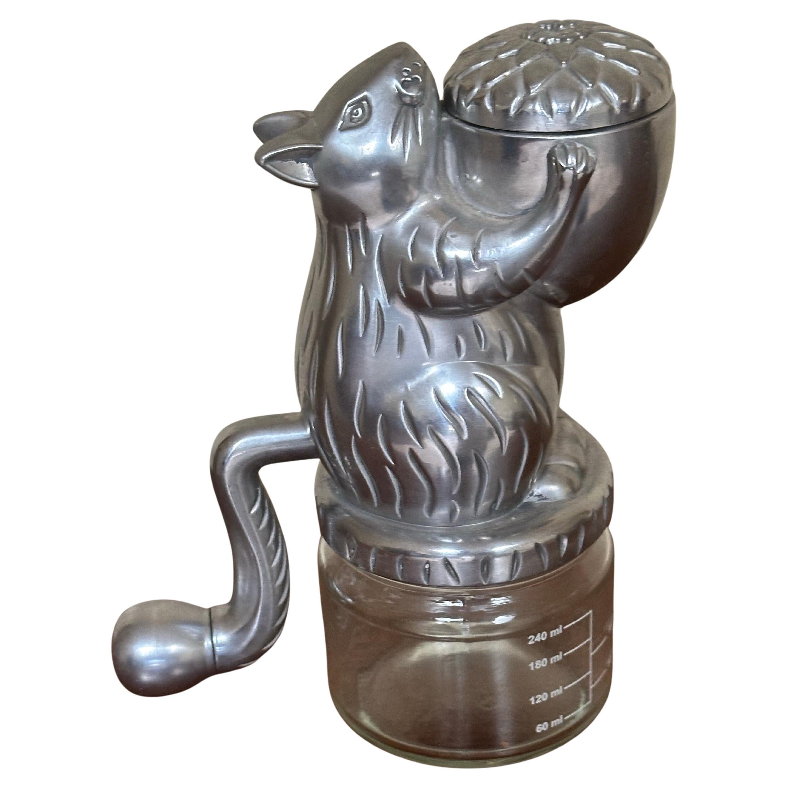 Vintage Inspired Squirrel Nut Grinder with Glass Measuring Cup & Hand Crank Tail, circa 2012. Made from stainless steel and glass, this device is designed to grind or chop nuts using the manual hand crank (the squirrel's tail) which activates the