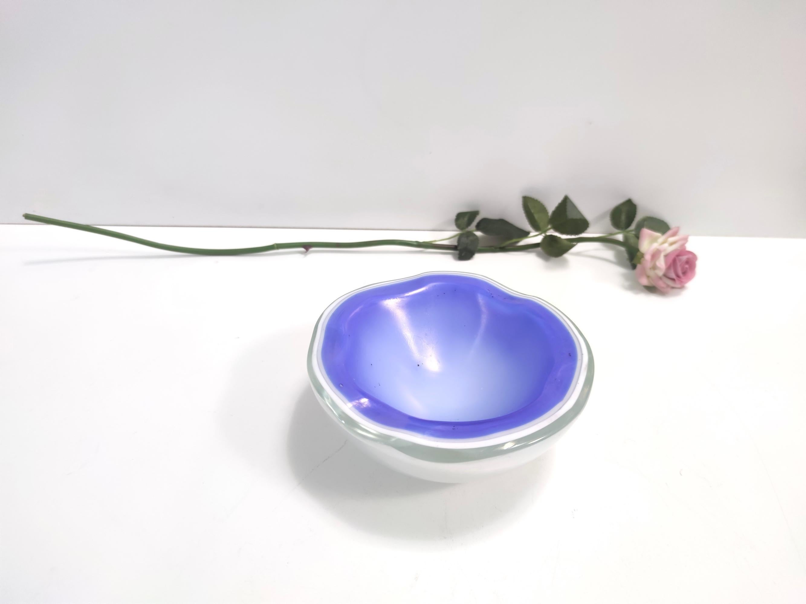 Made in Italy, Murano, 1950s- 1960s.
It is made in quite heavy 4-layered iridescent cornflower blue and white hand-blown glass. 
This trinket bowl / ashtray looks like a geode. 
It might show black impurities due to its old process: as a matter of