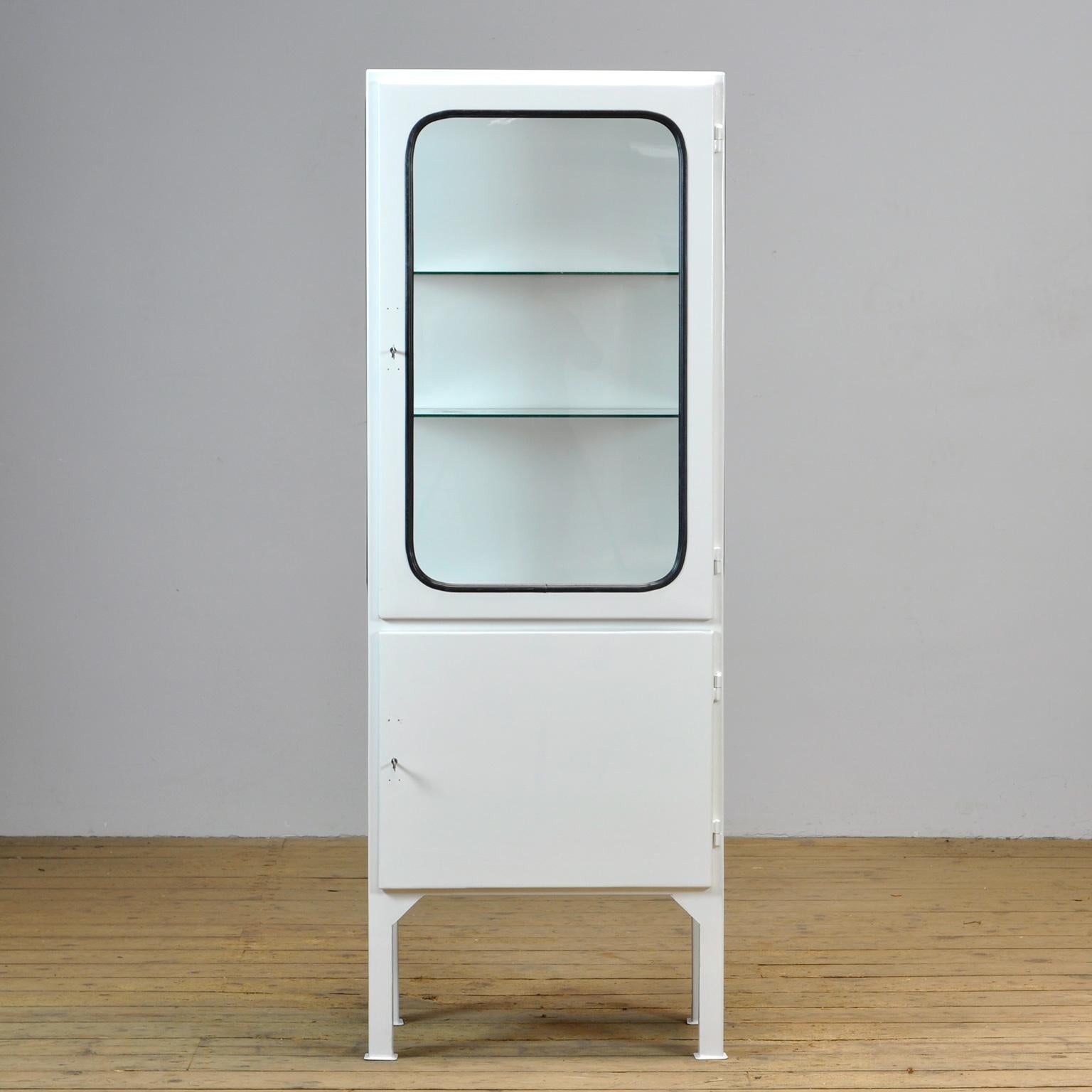 This medical cabinet was designed in the 1970s and was produced circa 1975 in hungary. It is made from iron and glass with new glass shelves. The glass is held by a black rubber strip. The cabinet features two adjustable glass shelves and