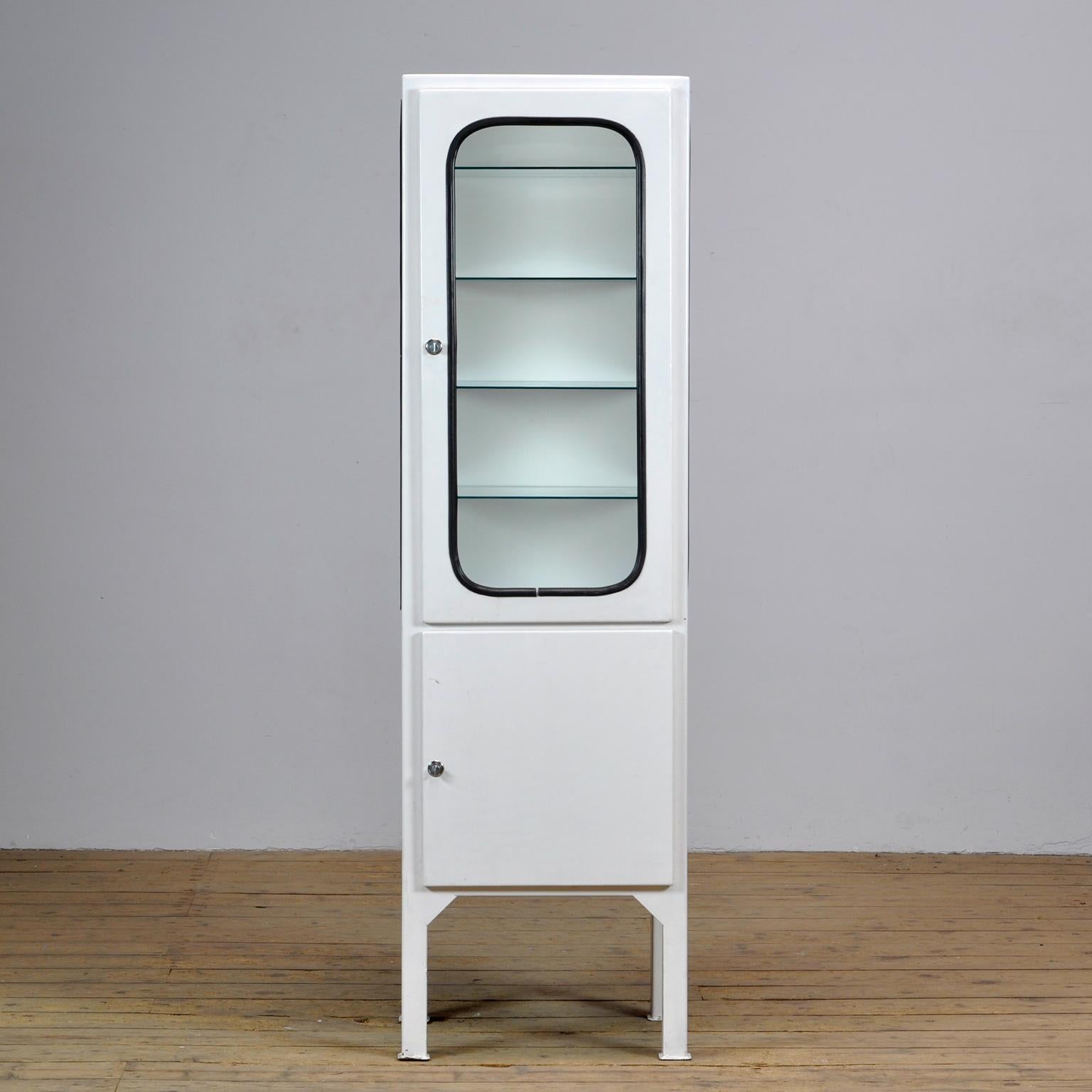 This medical cabinet was designed in the 1970s and was produced circa 1975 in hungary. It is made from iron and glass with new glass shelves. The glass is held by a black rubber strip. The cabinet features four adjustable glass shelves and