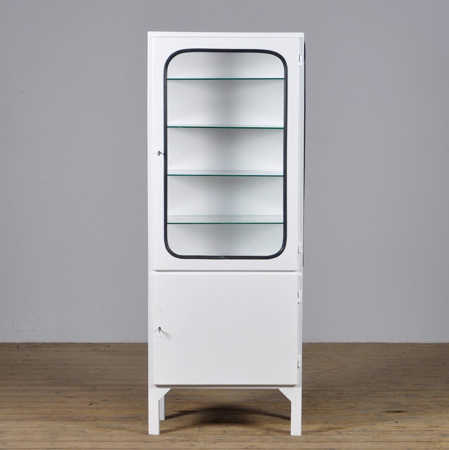 This medical cabinet was designed in the 1970s and was produced circa 1975 in hungary. It is made from iron and glass, and the glass is held by a black rubber strip. The cabinet features four adjustable glass shelves and a functioning lock. 