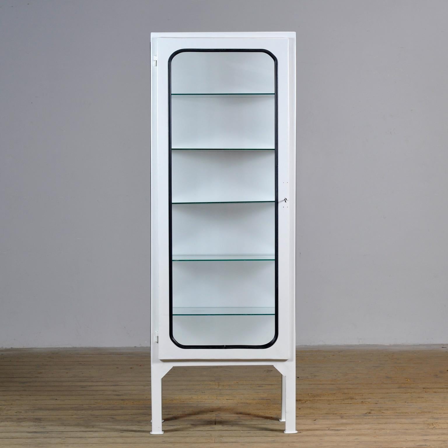 This medical cabinet was designed in the 1970s and was produced circa 1975 in hungary. It is made from iron and glass with new glass shelves. The glass is held by a black rubber strip. The cabinet features five adjustable glass shelves and a