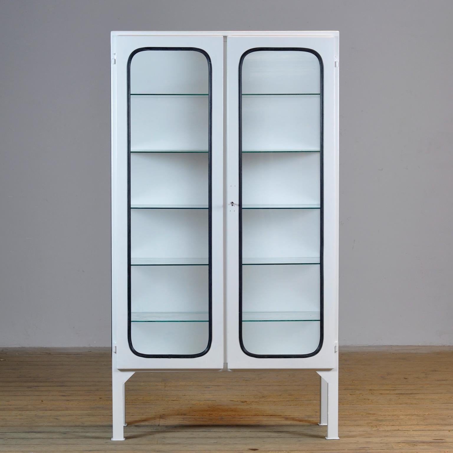 This medical cabinet was designed in the 1970s and was produced circa 1975 in hungary. It is made from iron and glass with new glass shelves. The glass is held by a black rubber strip. The cabinet features five adjustable glass shelves and a