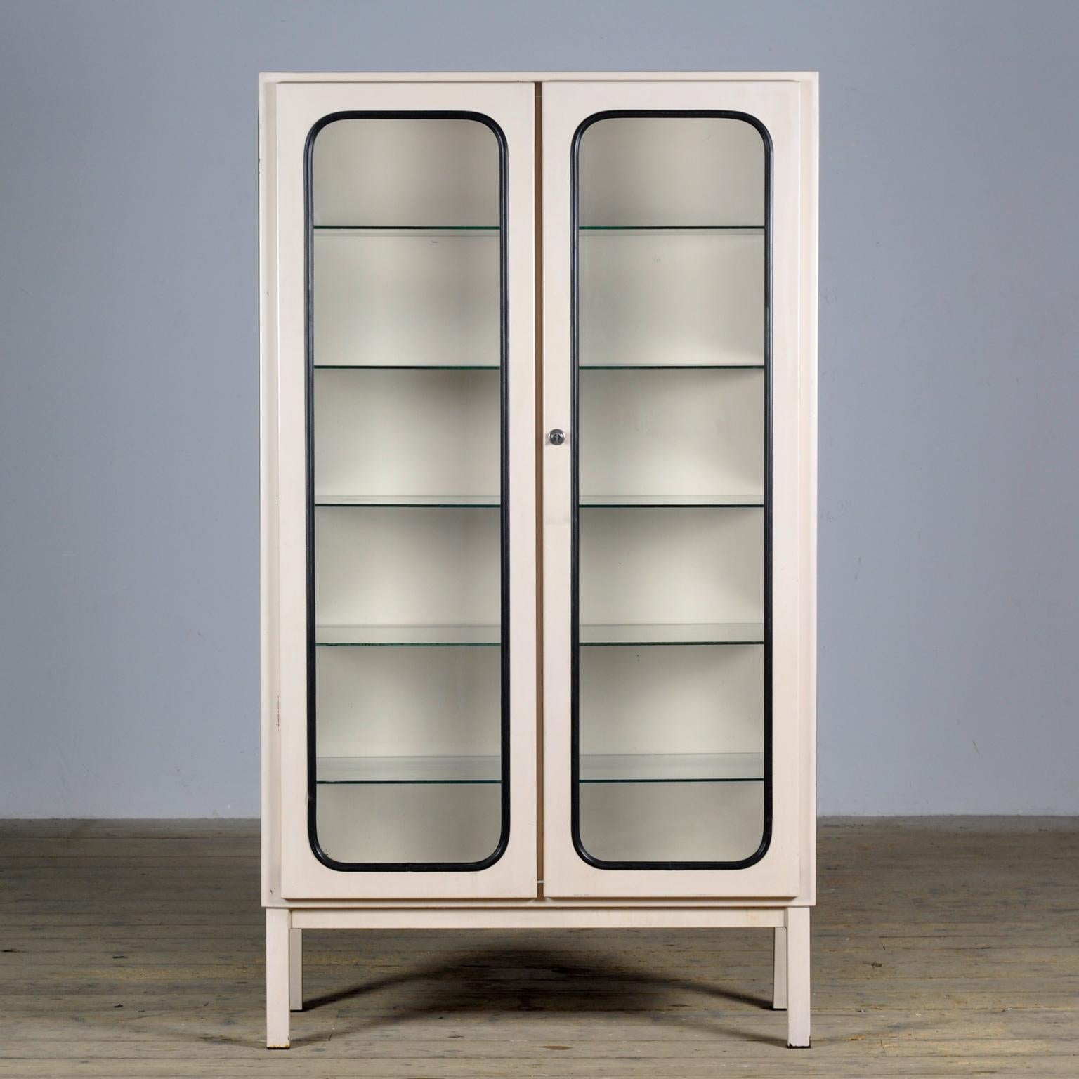 This medical cabinet was designed in the 1970s and was produced circa 1975 in hungary. It is made from iron and glass with glass shelves. The glass is held by a black rubber strip. The cabinet features five adjustable glass shelves and a functioning