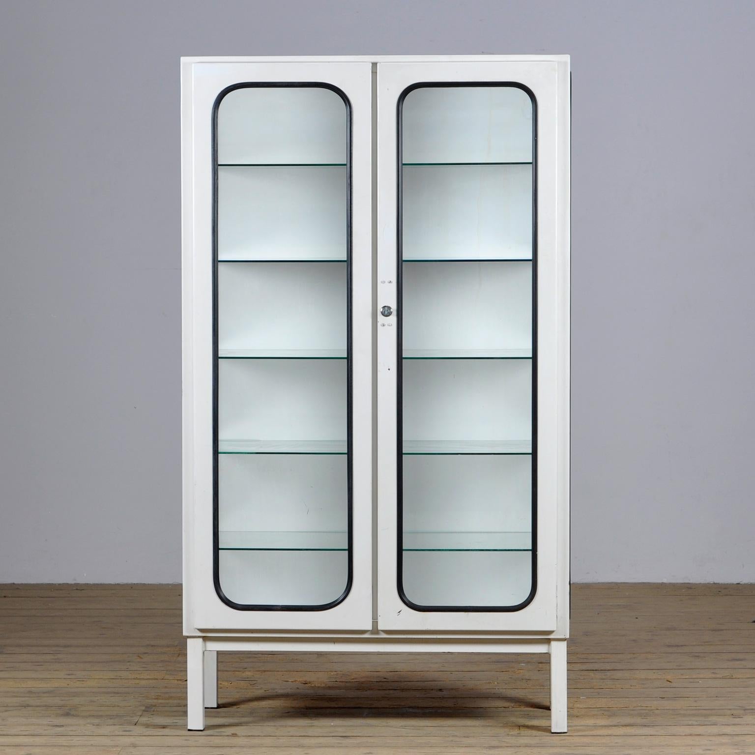 This medical cabinet was designed in the 1970s and was produced circa 1975 in hungary. It is made from iron and glass with glass shelves. The glass is held by a black rubber strip. The cabinet features five adjustable glass shelves and a functioning