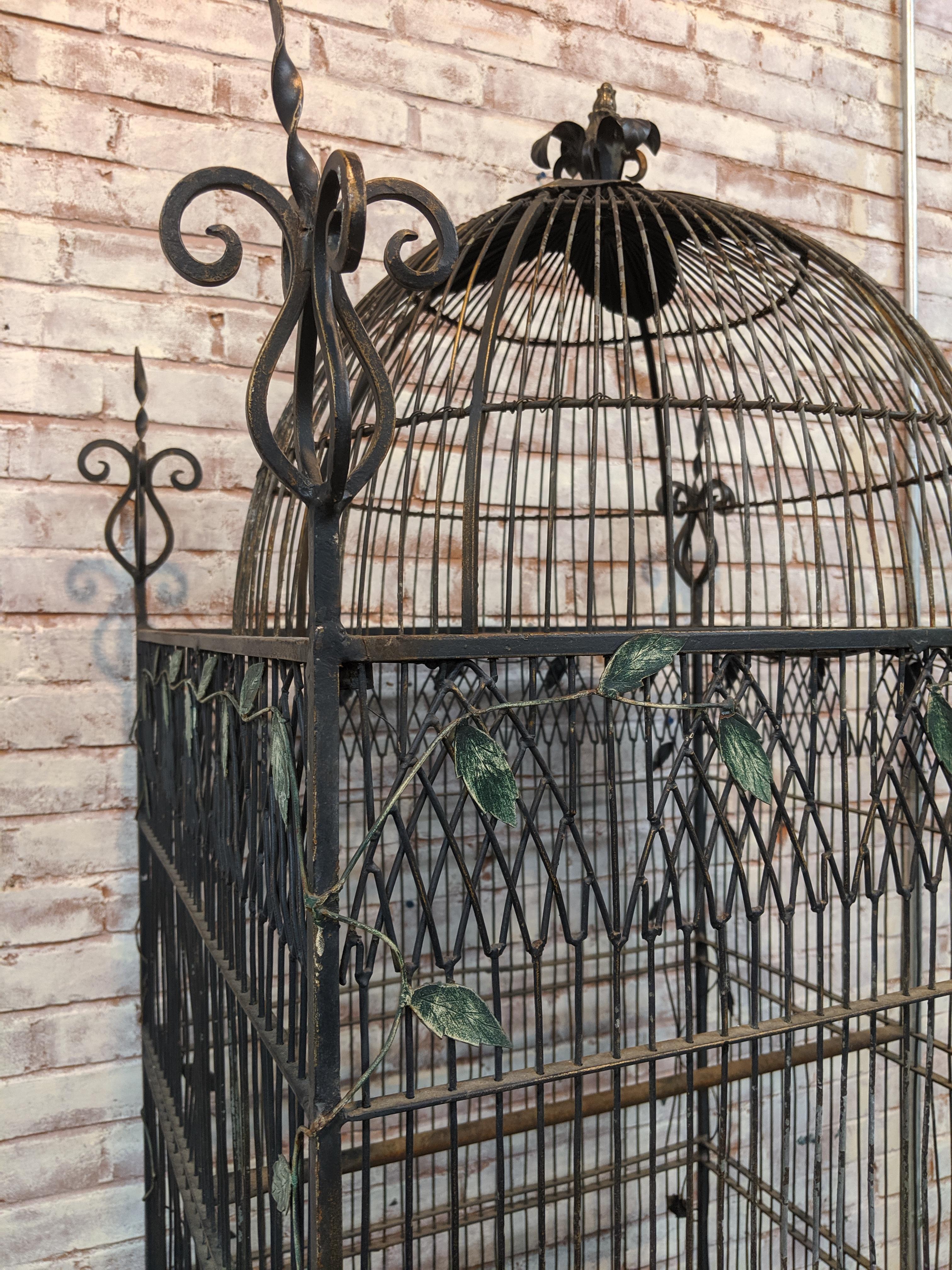 Beautiful wrought iron vintage birdcage. Cage is decorated with ornate finials at each corner and has a leaf motif all around the sides and top. Cage rests upon an ornate wrought iron stand. Base measures 27